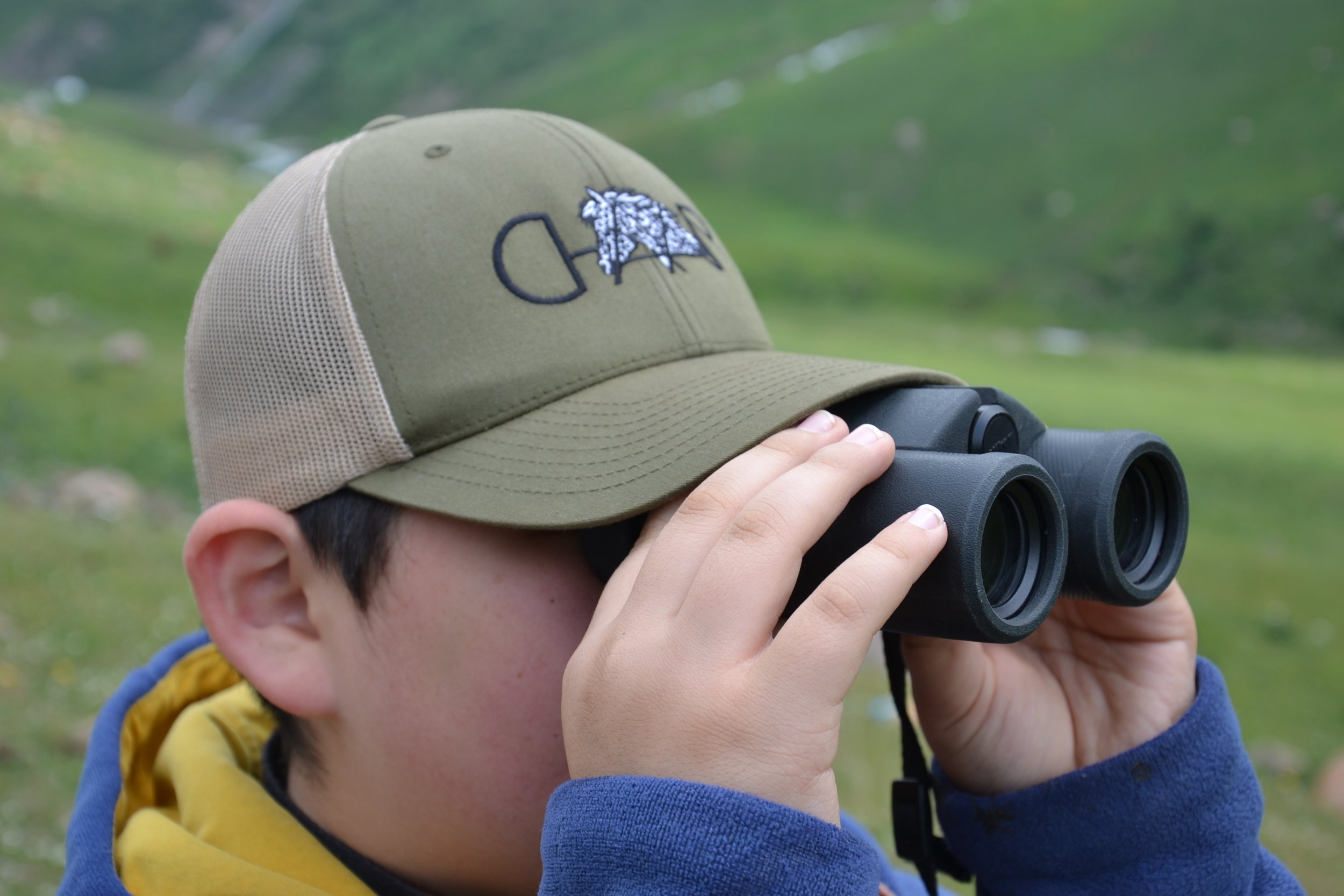 A boy wearing a cap looking through binoculars