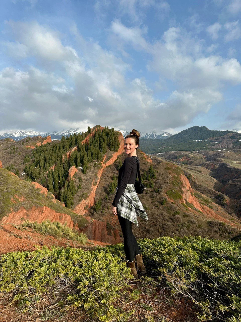 A woman posing on a ridge above red rock canyons and forested hills