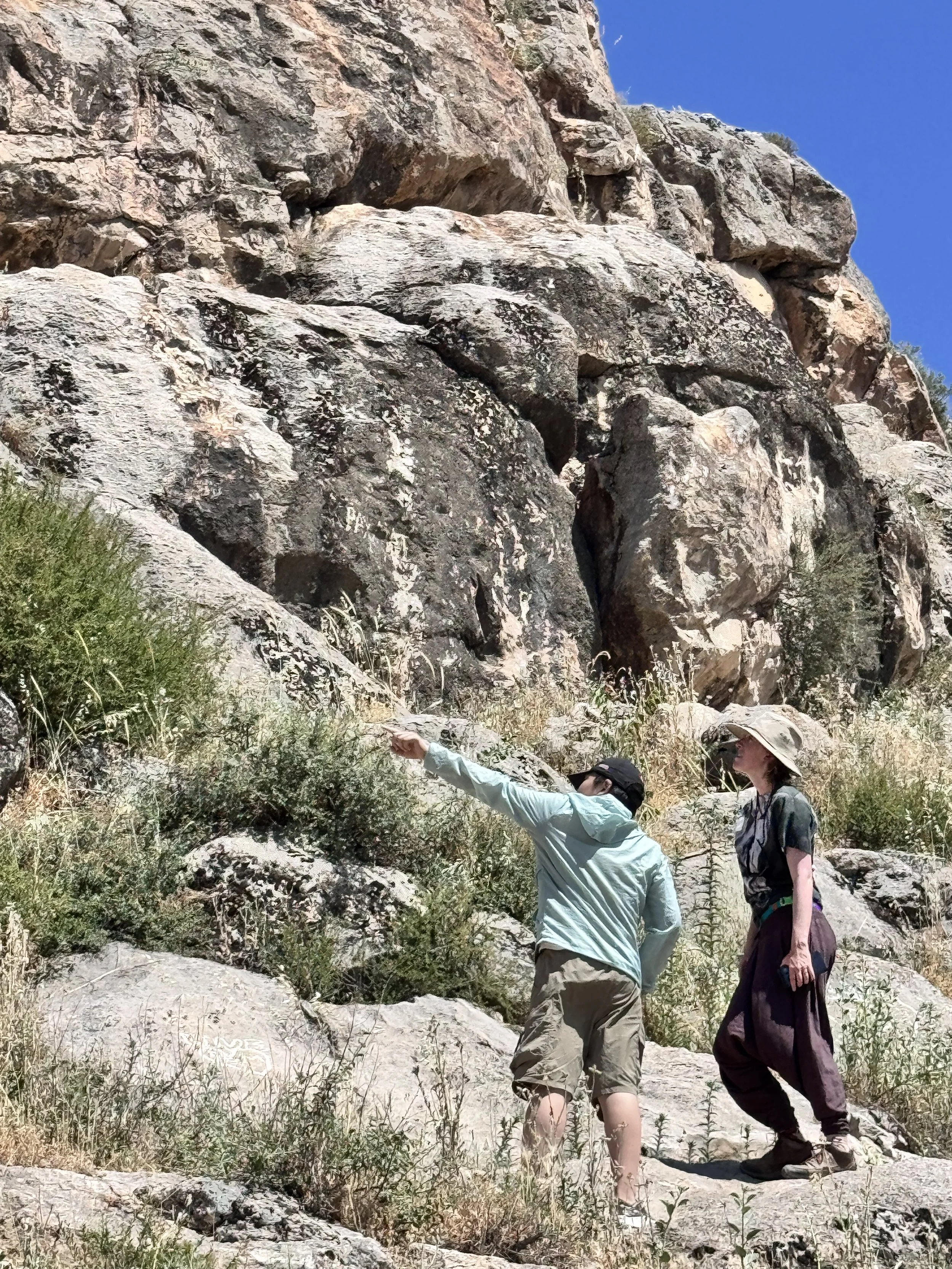 Two hikers examine a rocky cliff face while exploring