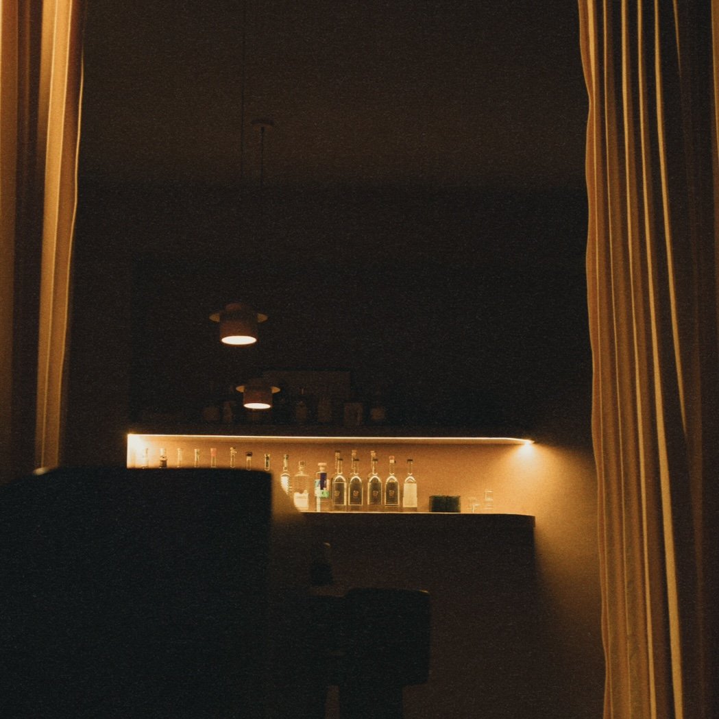 A dimly lit bar with bottles on a shelf behind the counter and curtains on either side of the opening.