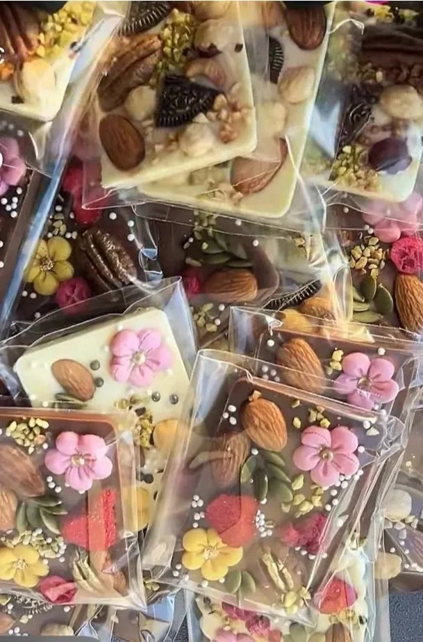 Assorted decorated chocolates and confections wrapped in clear plastic, decorated with colorful flowers, nuts, and edible pearls.