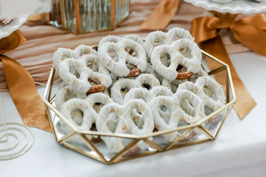 Close-up of pretzels drizzled with white icing and sprinkled with gold edible glitter, displayed on a gold tray.