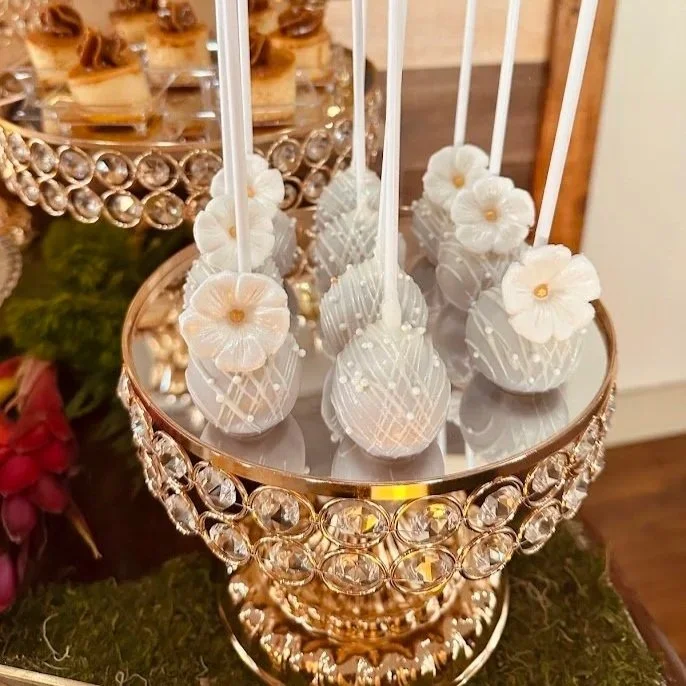 White cake pops decorated with flowers and drizzled with white icing on a golden stand.