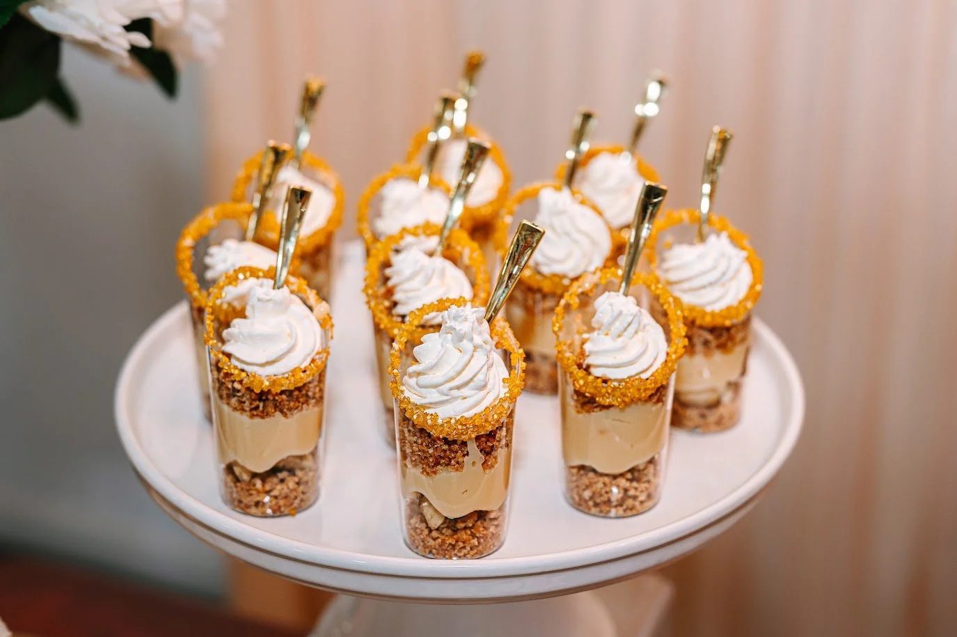 Four small glass cups with layered dessert and whipped cream on top, set on a decorative gold stand.