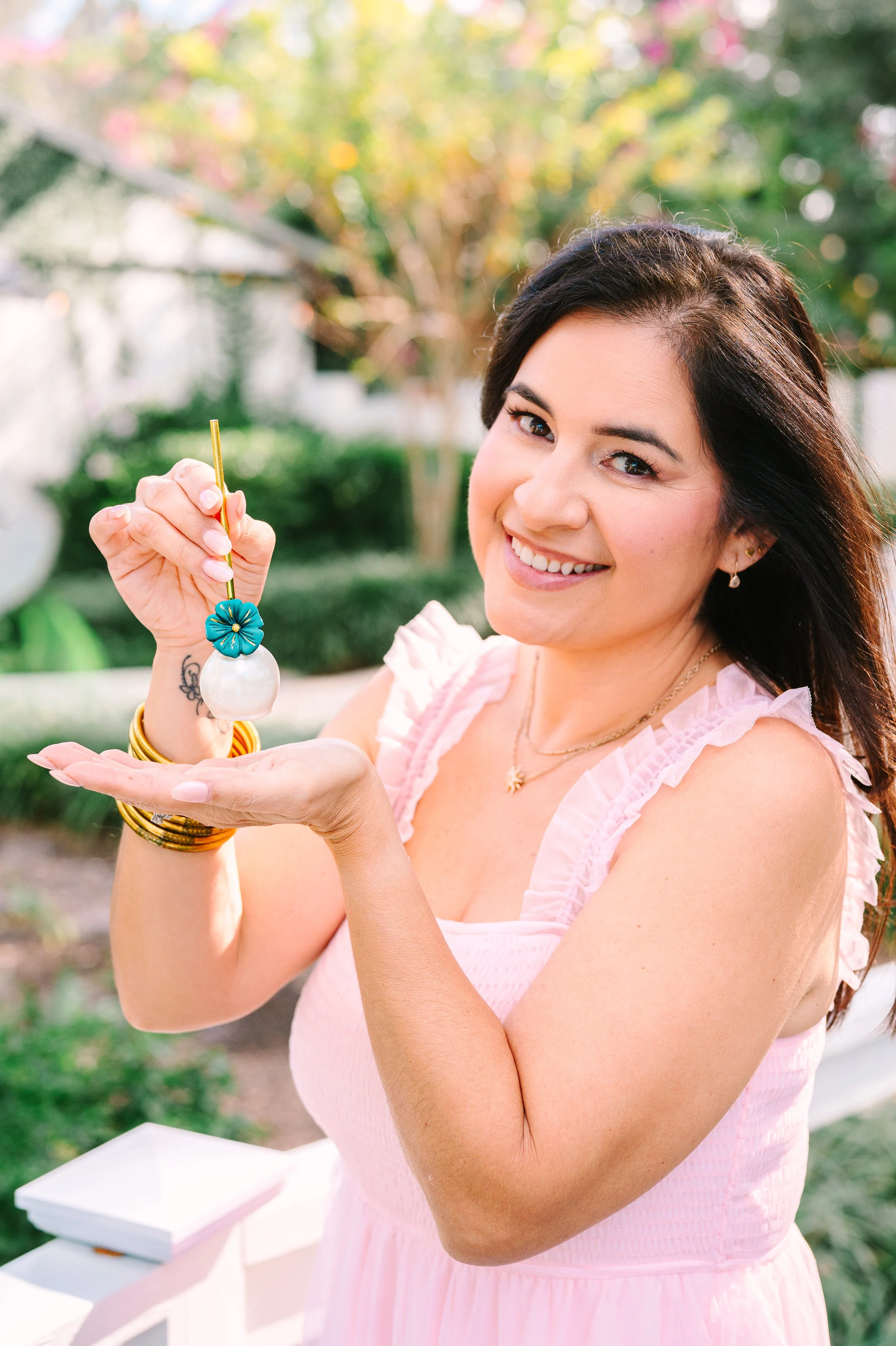 Woman holding a pearl dessert with a decorative flower stick, smiling outdoors in a garden setting.