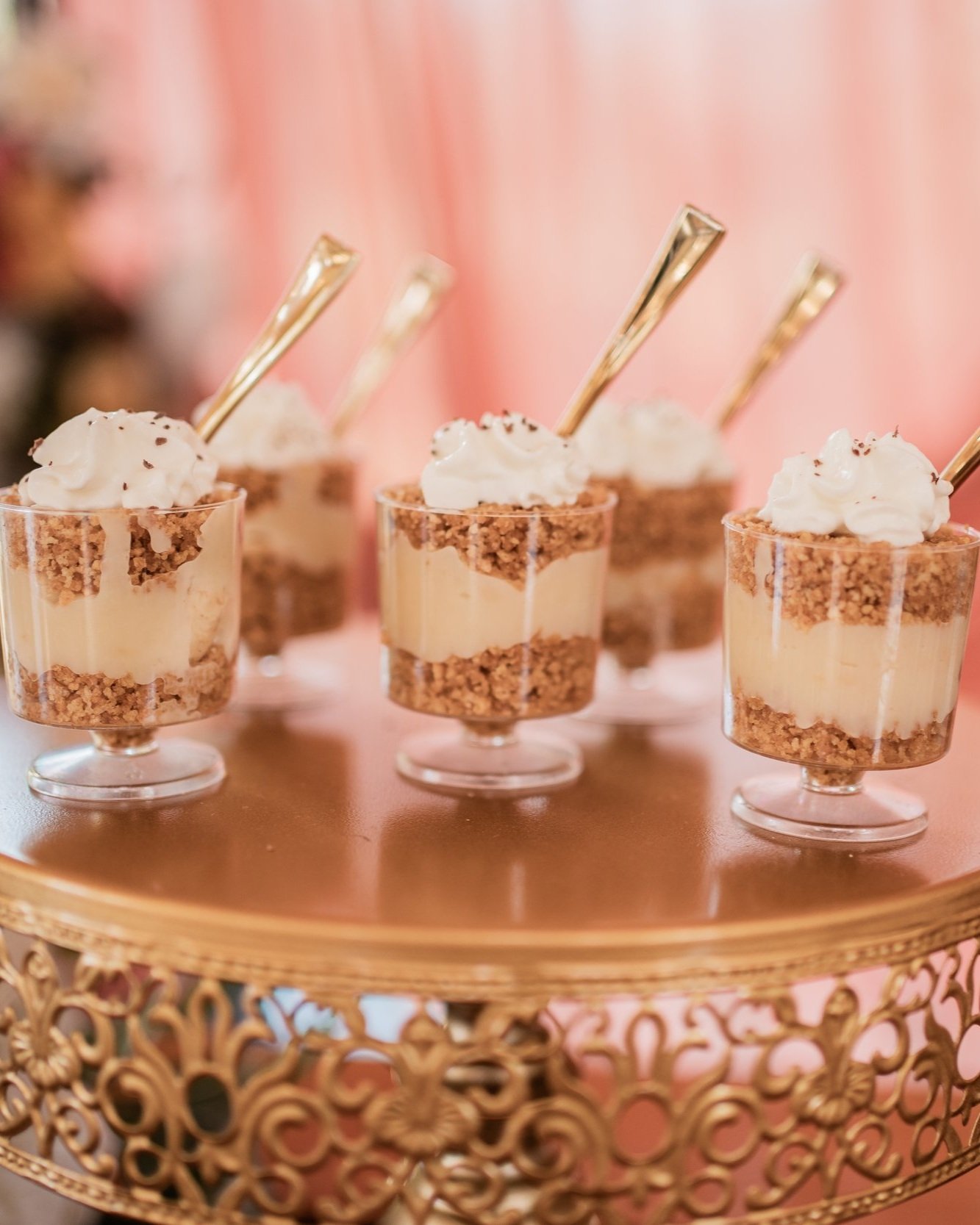 Mini dessert parfaits with layers of crushed cookies, creamy filling, topped with whipped cream and chocolate sprinkles, served in small glass cups on a decorative gold tray.