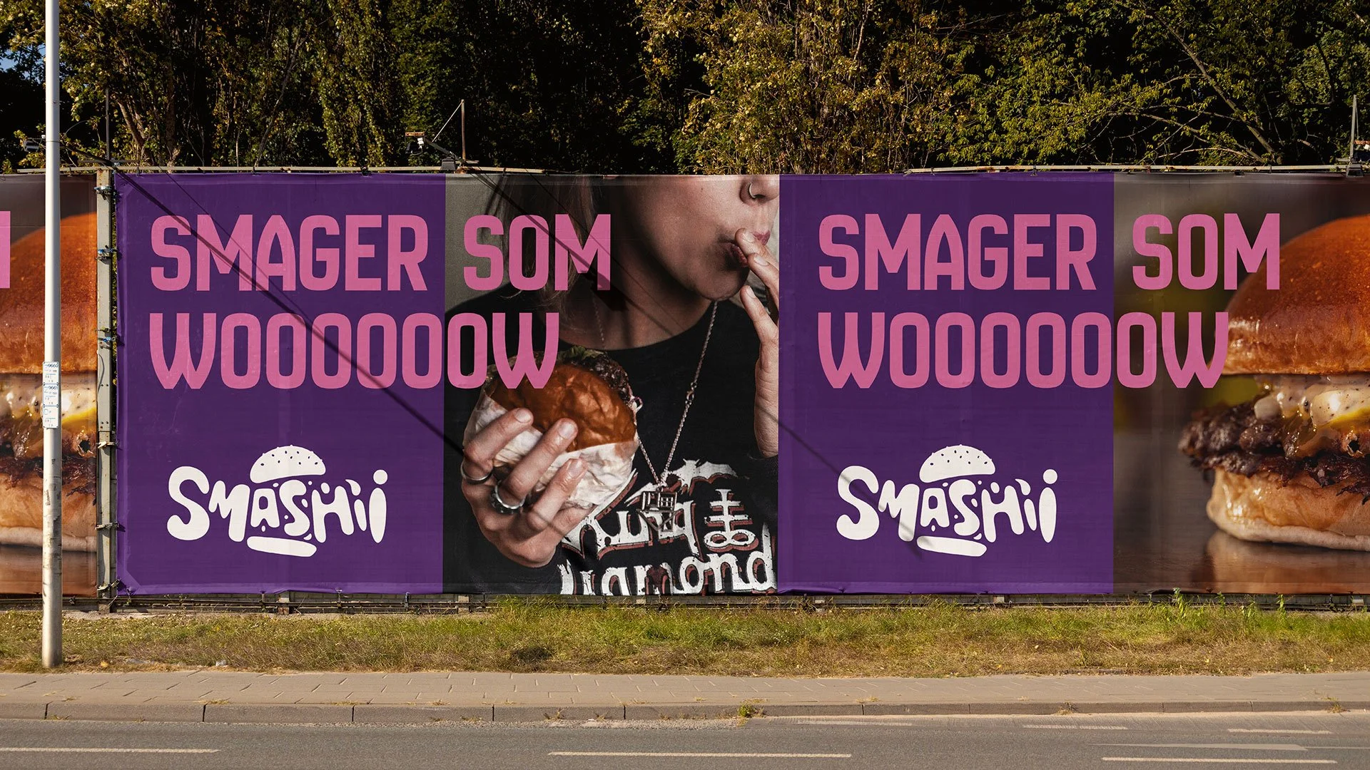 Billboard med billede af en kvinde, der spiser en burger, og teksten "Smager som woooow" og logoet "Smash'i".