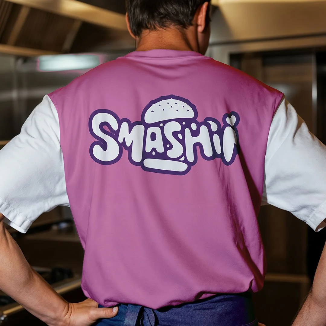 Bagperson med en pink køkkenforklæde med teksten "SMÅSHI" og en burgertegning på ryggen.
