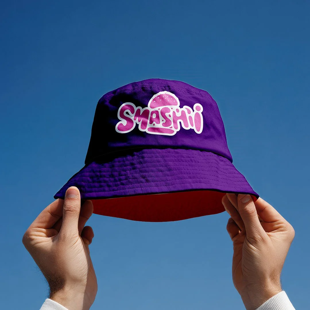Person holder en lilla hue med logoet 'SMASHI' mod en klar blå himmel.