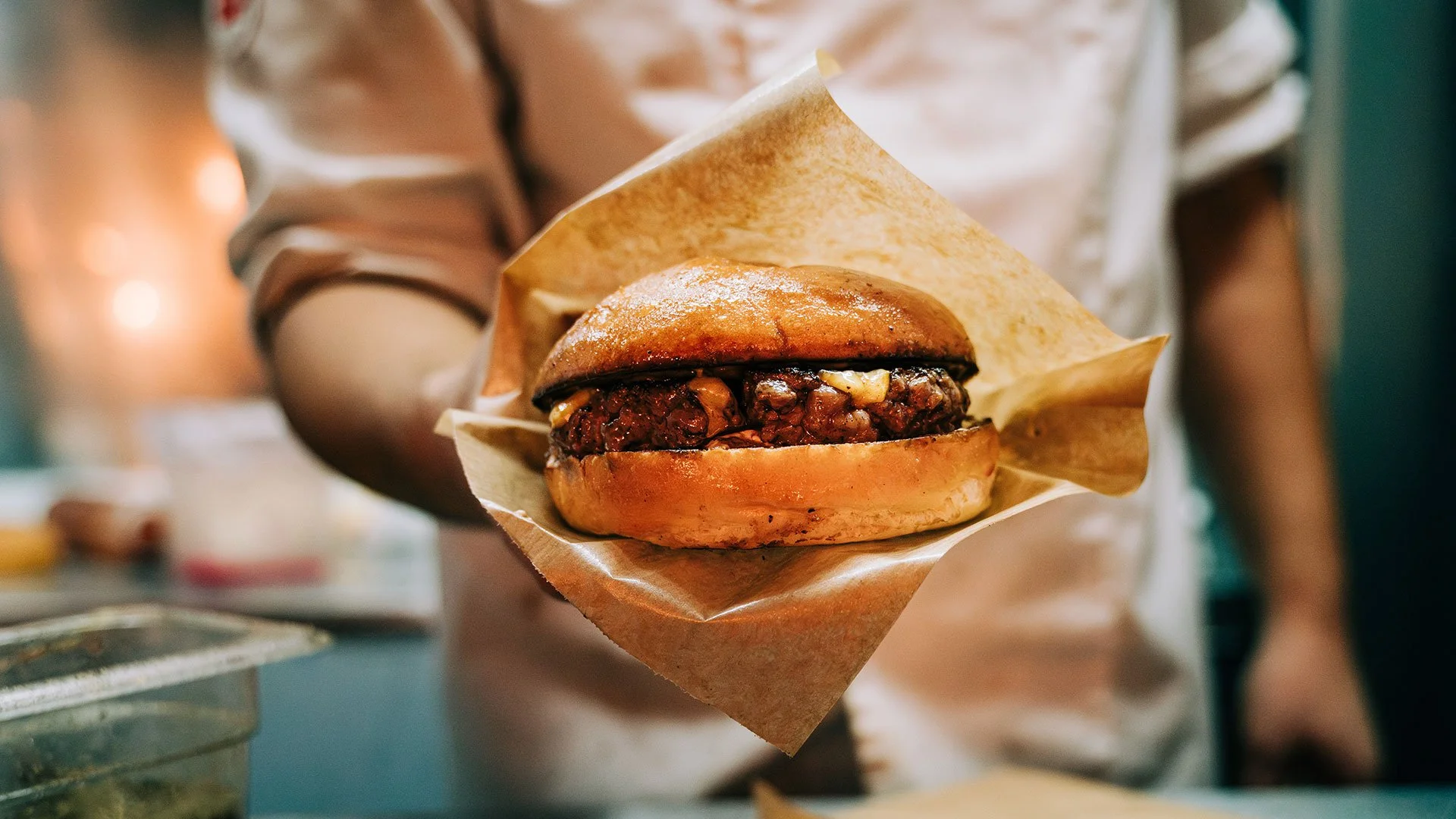 En person holder en burger med pulled pork og bbq-sauce, indpakket i brunt papir.