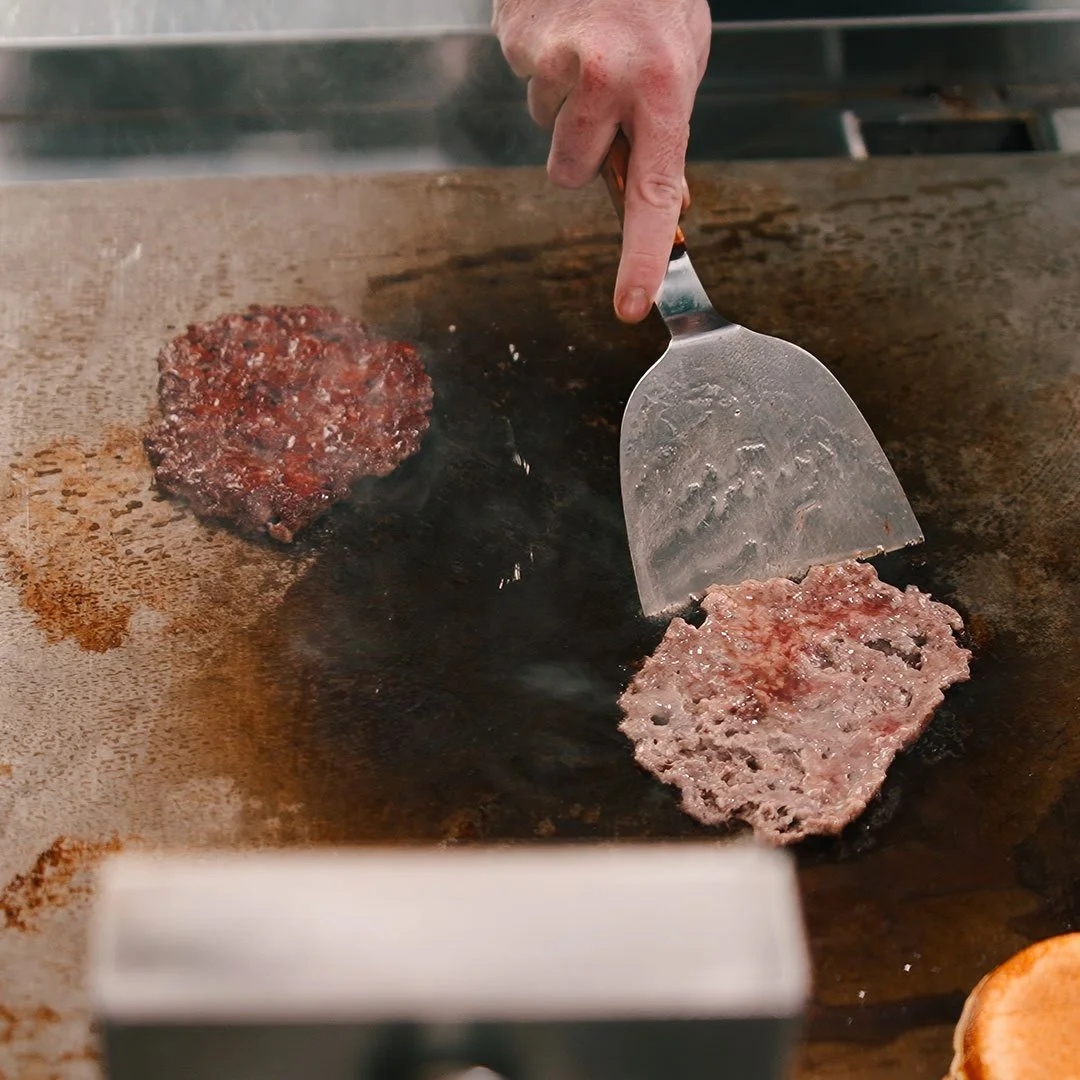 En person steger bøf på en grillpande med en flad skovl.