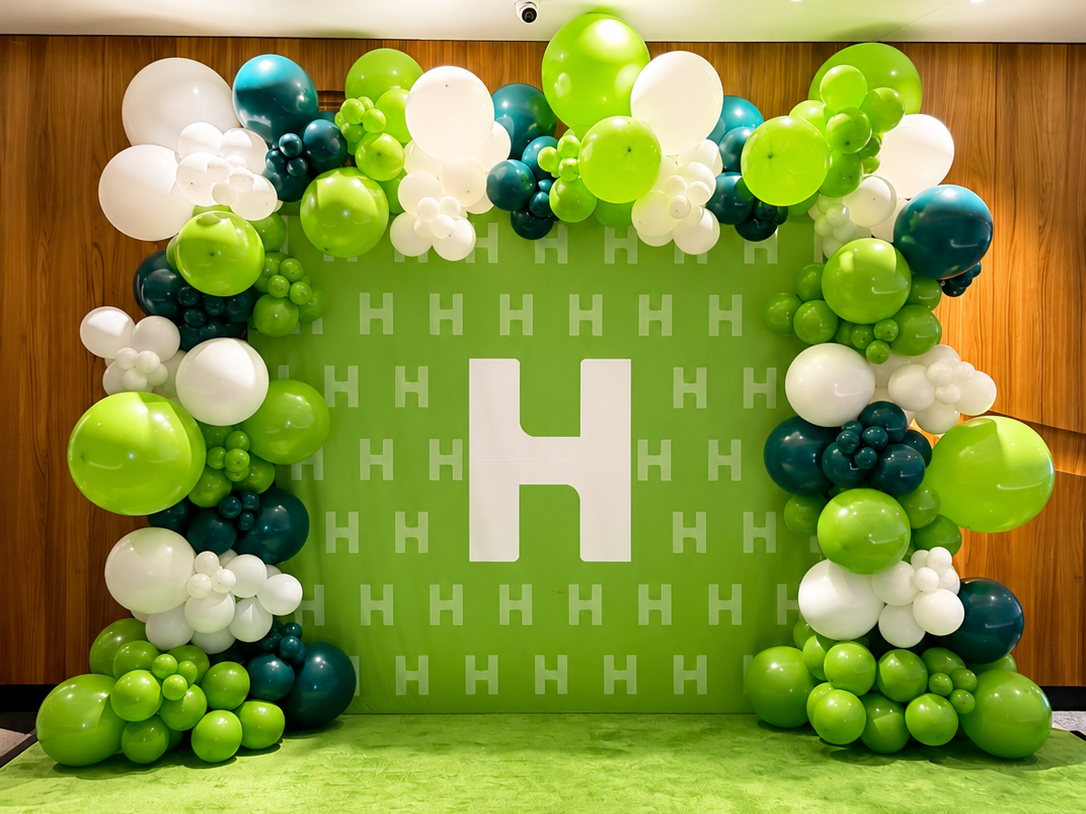 Decorative balloon wall with green, white, and dark teal balloons around a green background with a large white letter H
