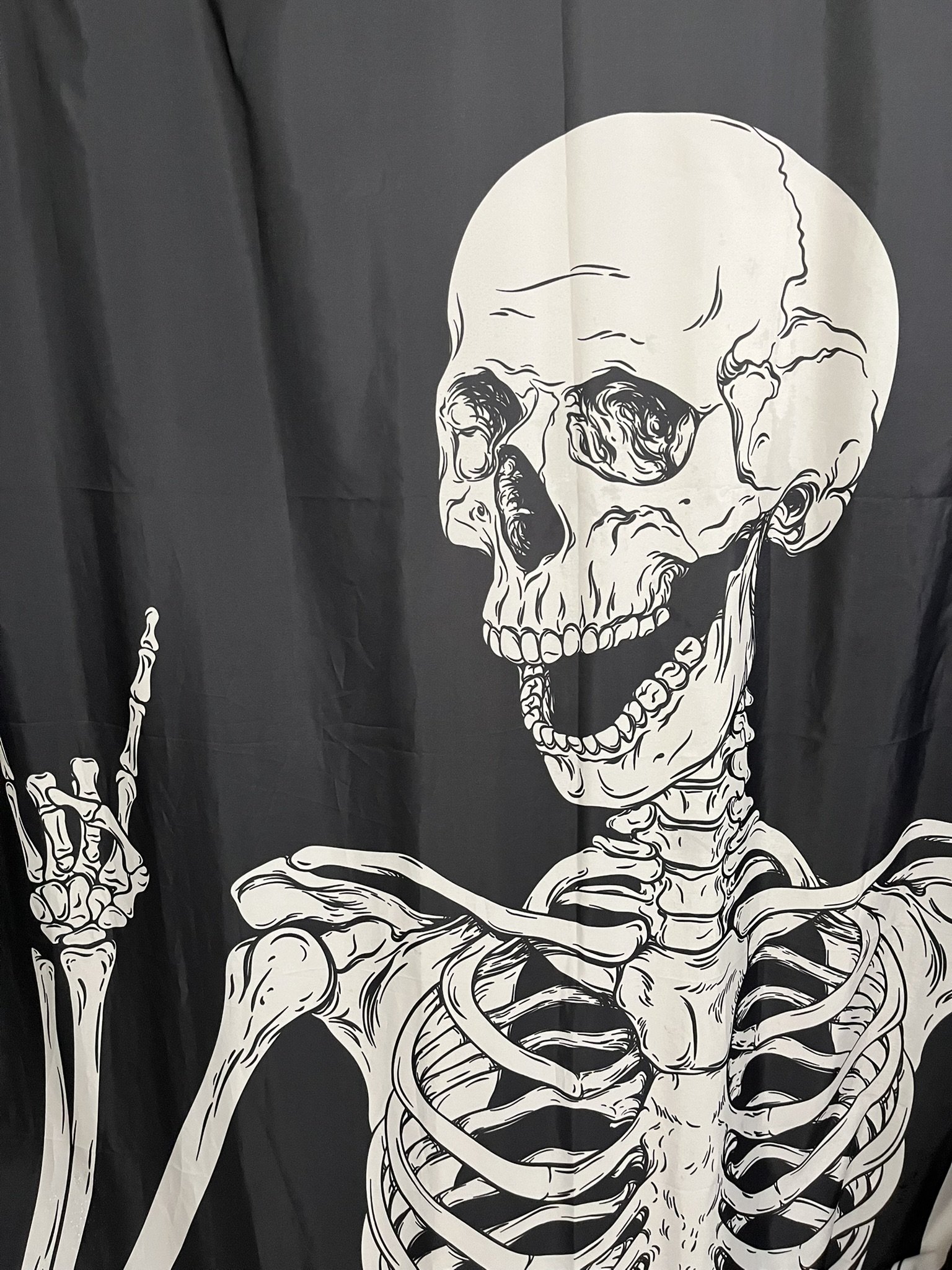 Black and white skeleton illustration with a smiling skull, holding up one finger, against a dark background.
