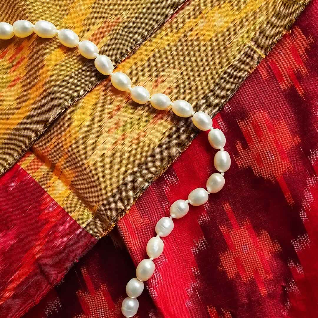 Photo of a white pearl necklace on top of a red and gold fabric for Pearl & Bead Restringing service at Patronik Designs Fine Jewlery in Burlingame, CA.