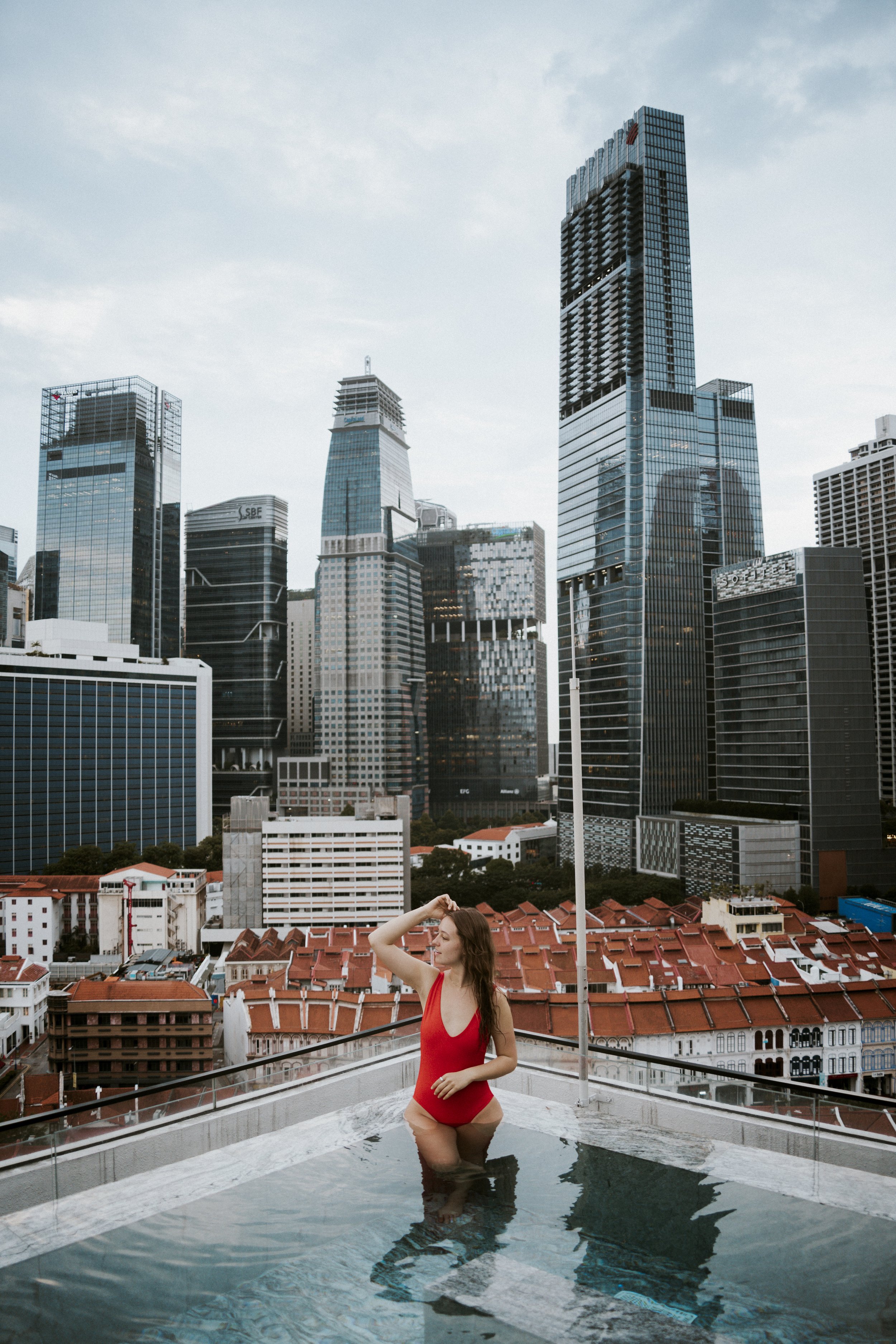 A woman in a red swimsuit standing in a rooftop pool with a city skyline in the background.