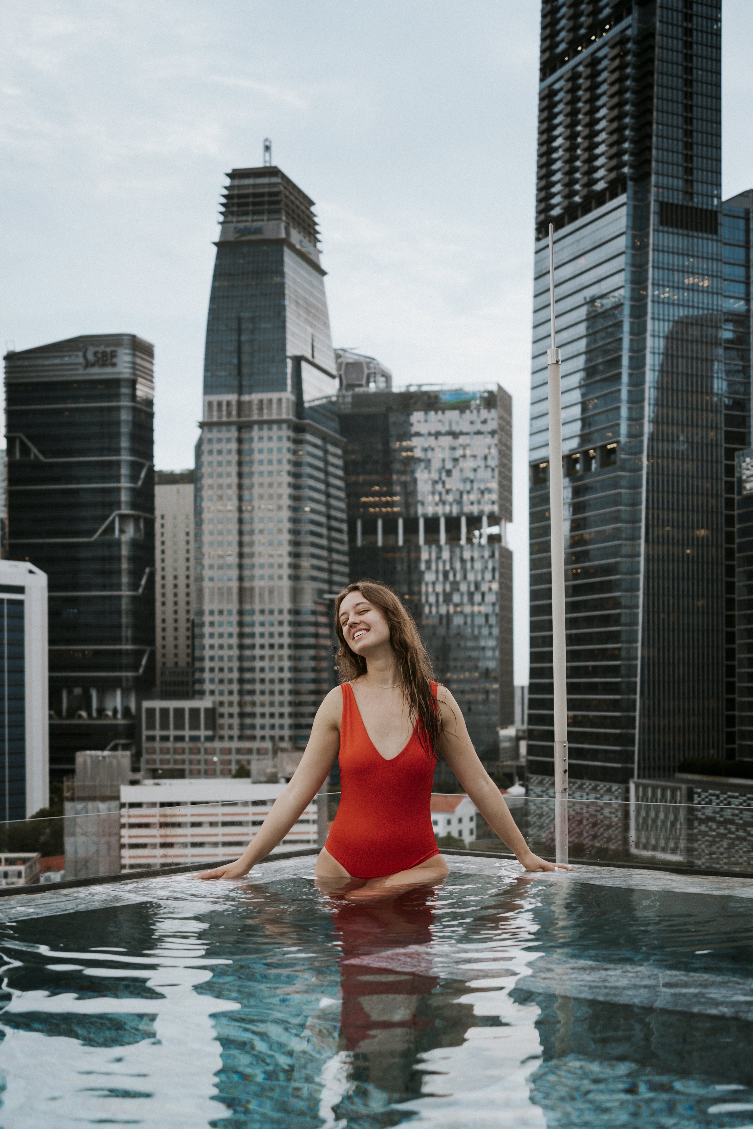 Woman in red swimsuit smiling in rooftop pool with city skyline