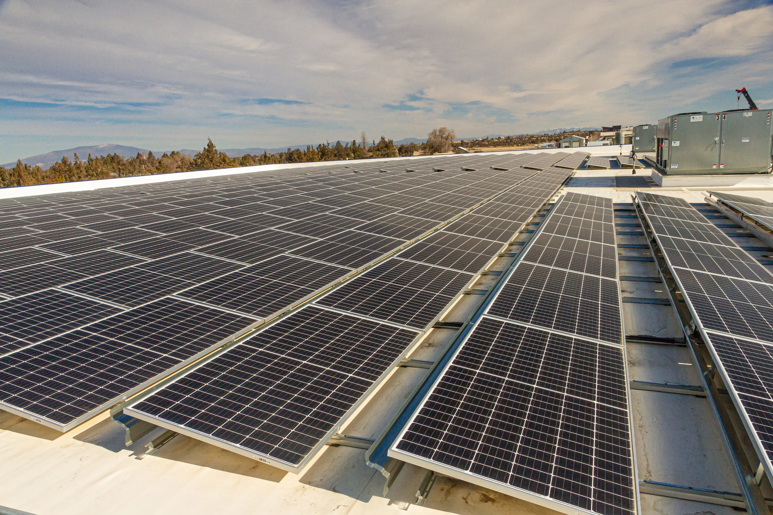 Multiple rows of solar panels installed on a flat rooftop with a partly cloudy sky in the background.