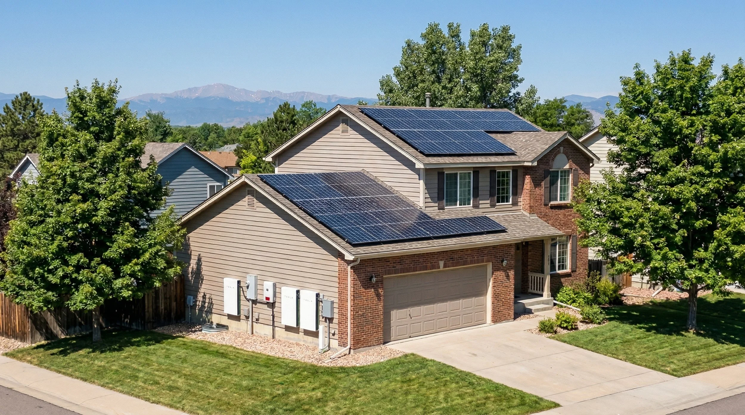 A two-story house with solar panels on the roof, a garage, and trees in the yard, with mountains in the background.