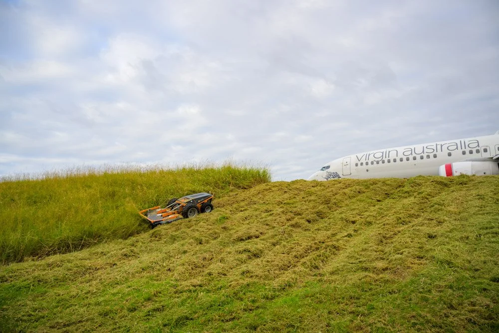 A toy car is rolling down a grassy hill with an airplane in the background that has 'Virgin Australia' written on it.