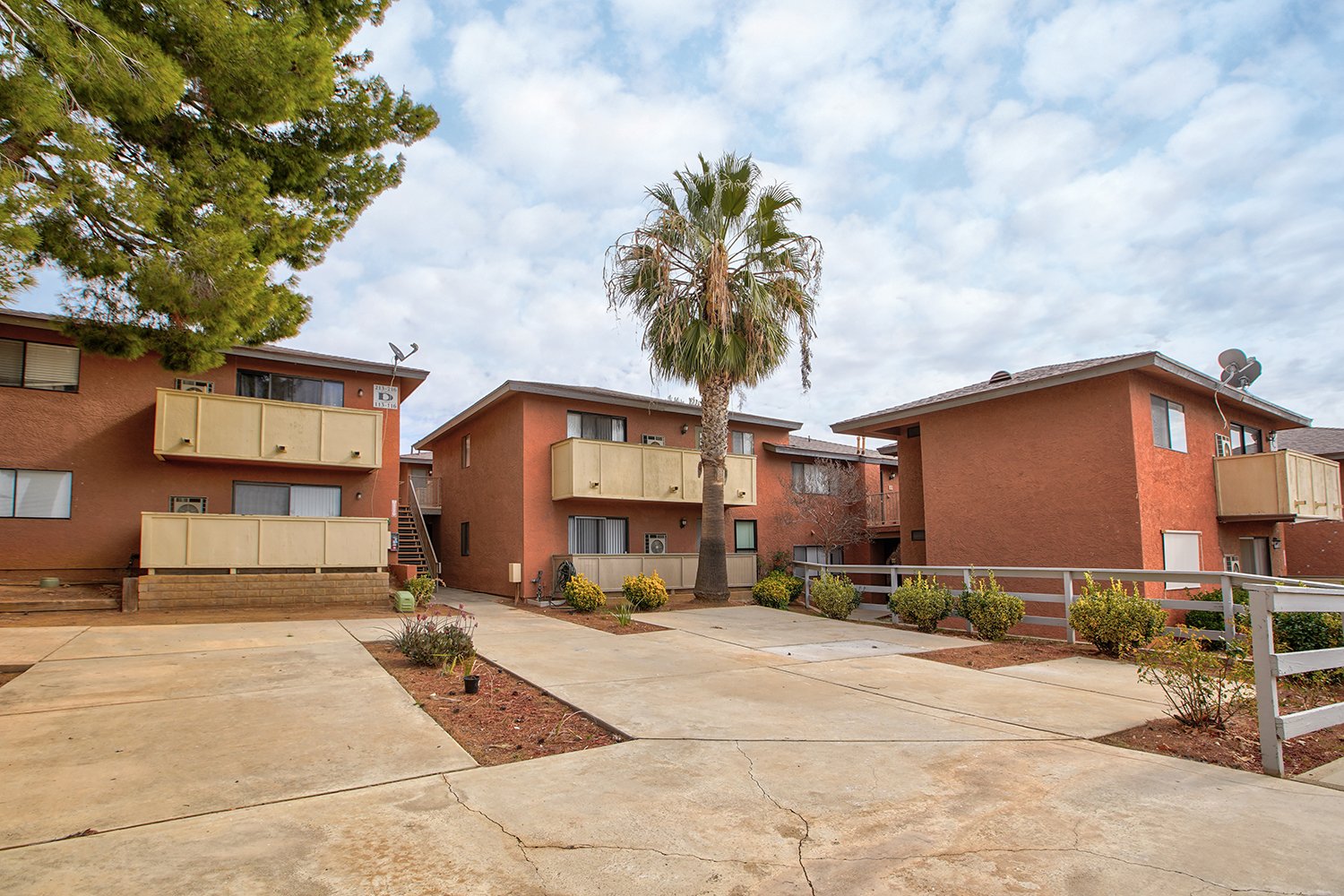 This image shows another angle of the two-story buildings featuring balconies and walkways framed by a large tree and a tall palm tree.