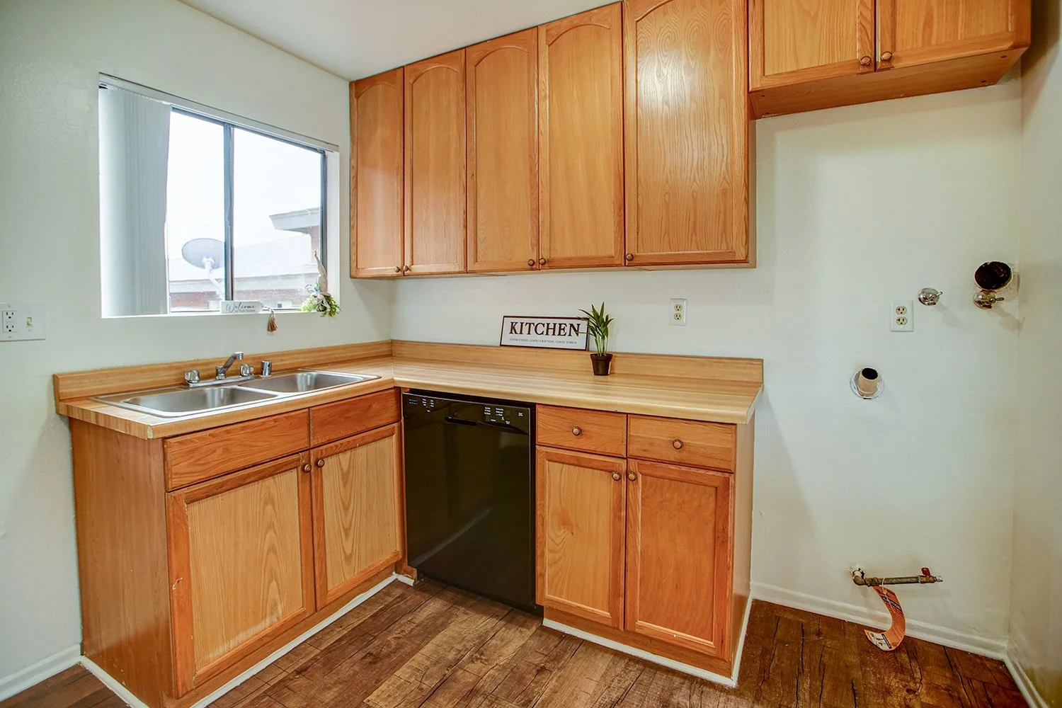 This image shows wooden kitchen cabinets with a double sink and an area for a fridge.