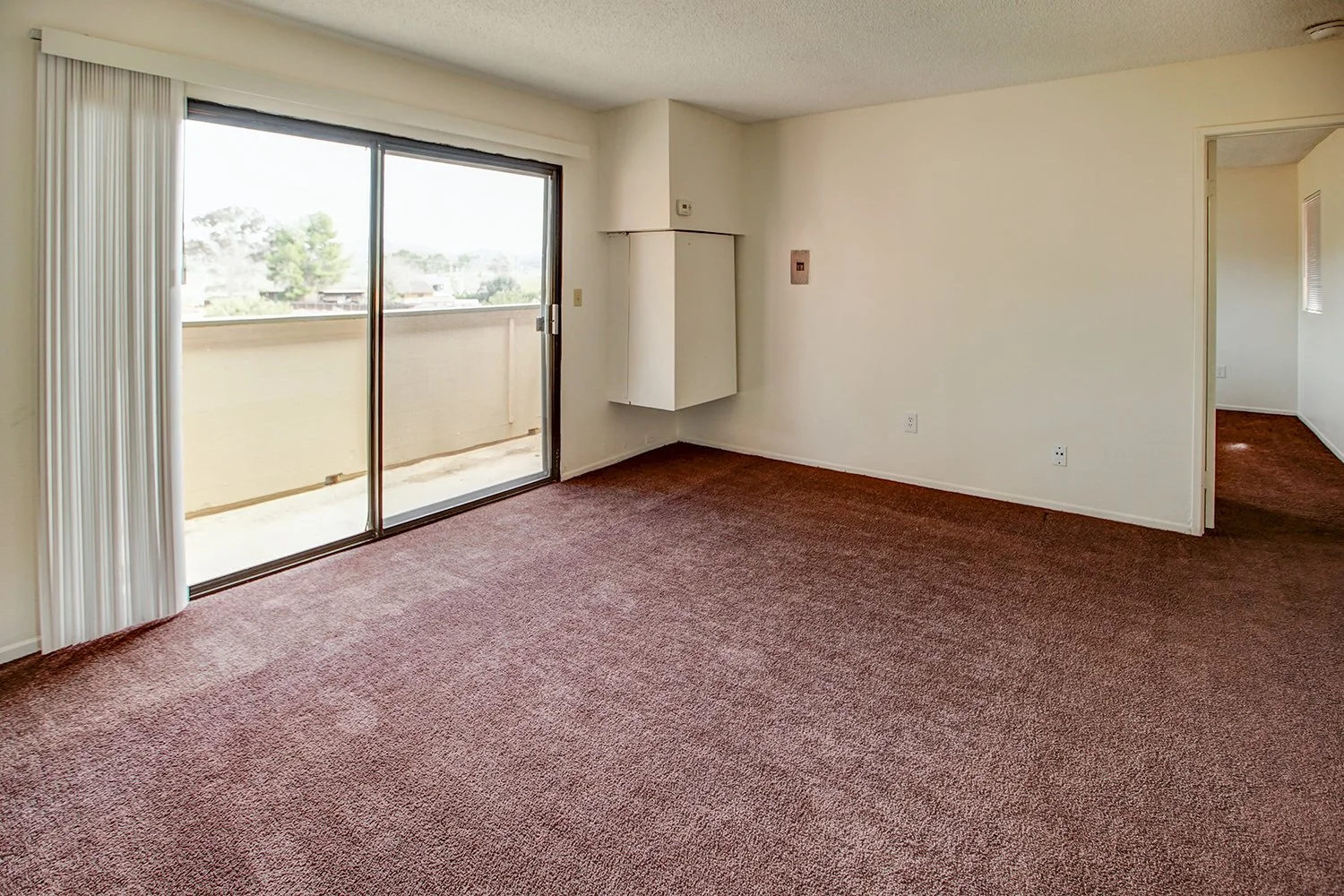 This image includes a look into a bedroom with carpeted flooring and a balcony.