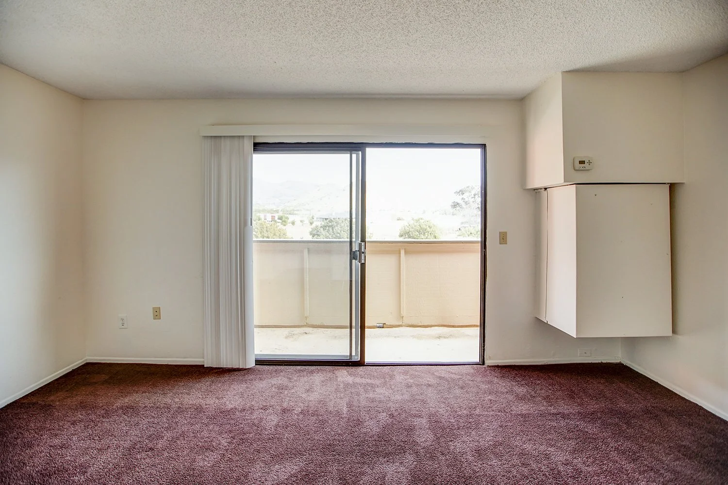 This image includes a look into a bedroom with carpeted flooring and a balcony.