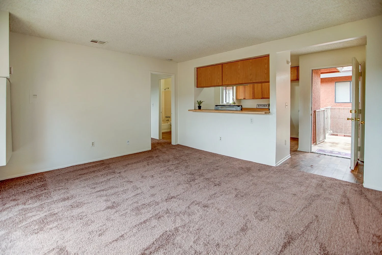 This image shows the carpeted living room and wood-floored kitchen. 