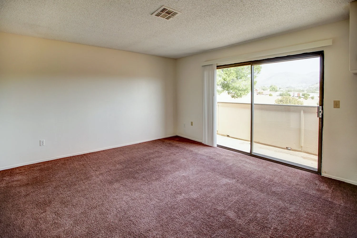 This image includes a look into a bedroom with carpeted flooring and a balcony.