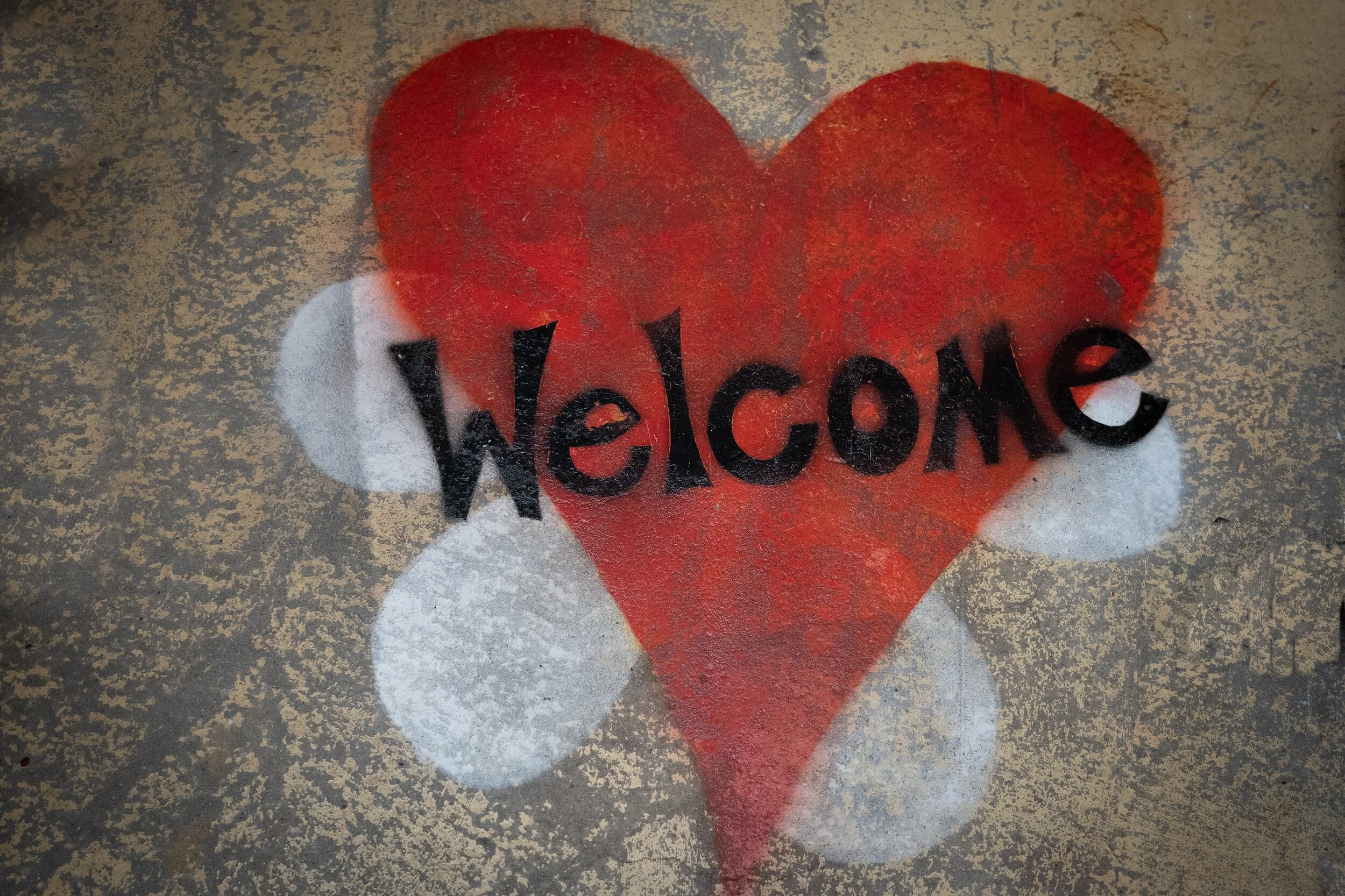 A spray-painted red heart with the word 'Welcome' painted over it on a concrete surface.