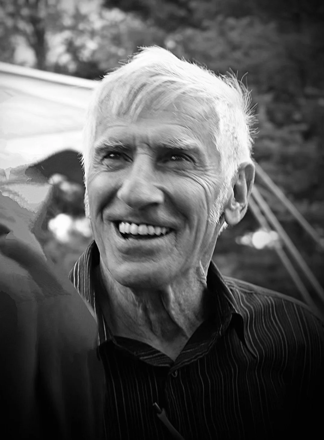 A black and white photo of an older man with white hair smiling outdoors.