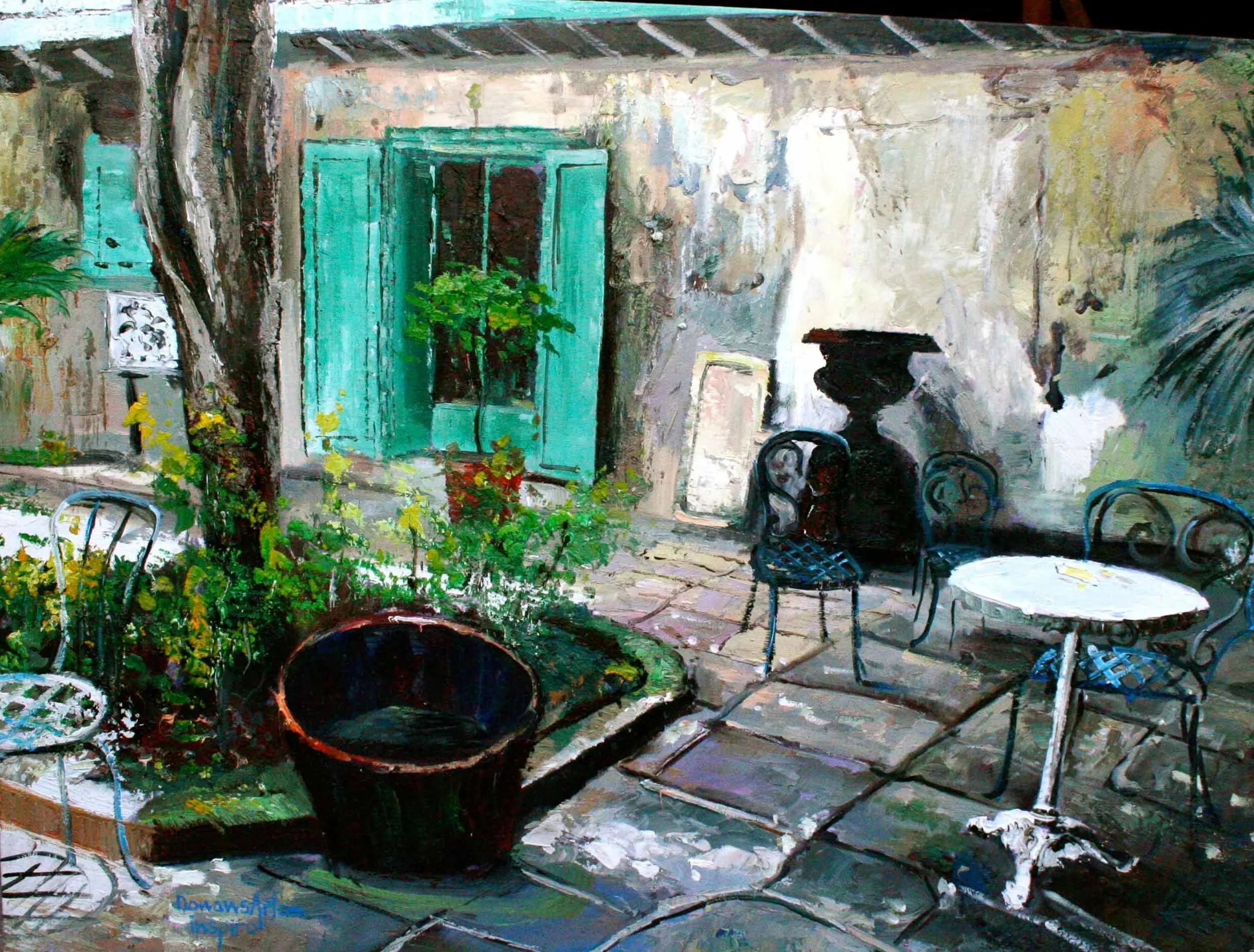 An outdoor patio scene with three black chairs, a glass-topped round table, large black pots, green plants, and a wall with turquoise shutters and a small decorative window. There are trees and plants in the background and a shaded roof overhead.