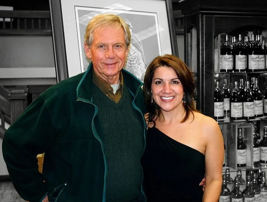 Robert Bateman and Michelle Boulanger standing together indoors, smiling for the camera in front of a display of bottles on shelves.
