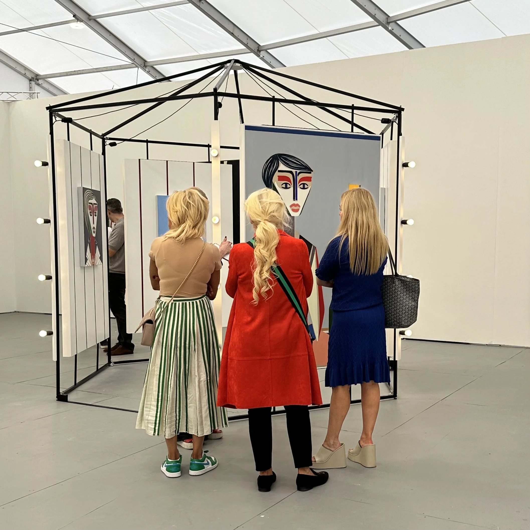 People standing in front of a decorative mirror with light bulbs, engaging in conversation at an indoor event.