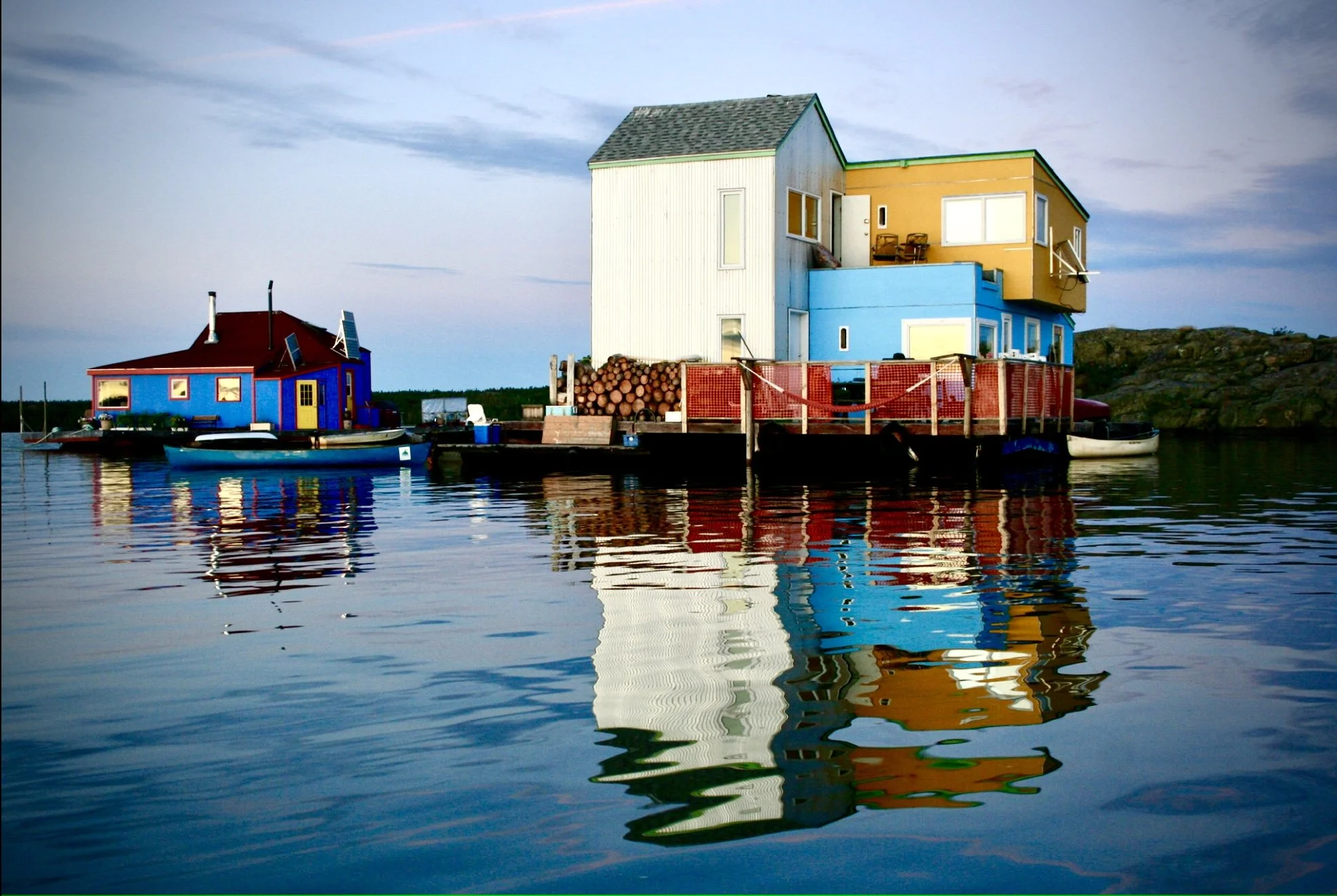 Colorful houseboat with multiple levels and balconies, floating on calm water, with sky and land in the background.