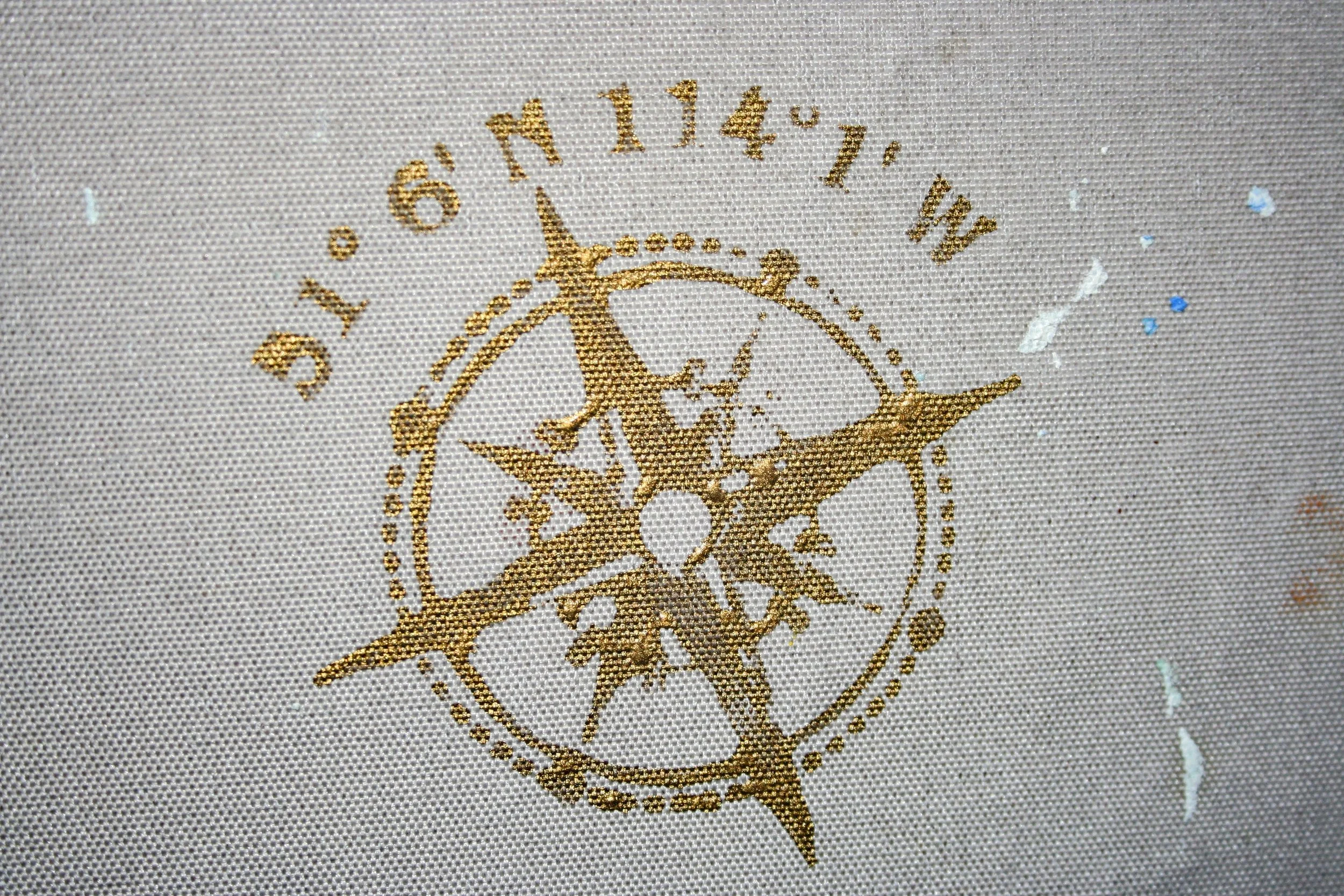 Close-up of a fabric with a printed design in gold ink, featuring a compass rose and circular decorative elements.