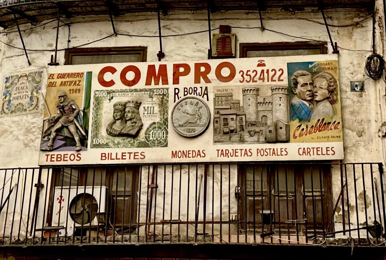 Sign advertising the sale of collectibles like stamps, tickets, coins, postcards, and posters, with historical images and artwork on an outdoor wall with a balcony and metal railing.