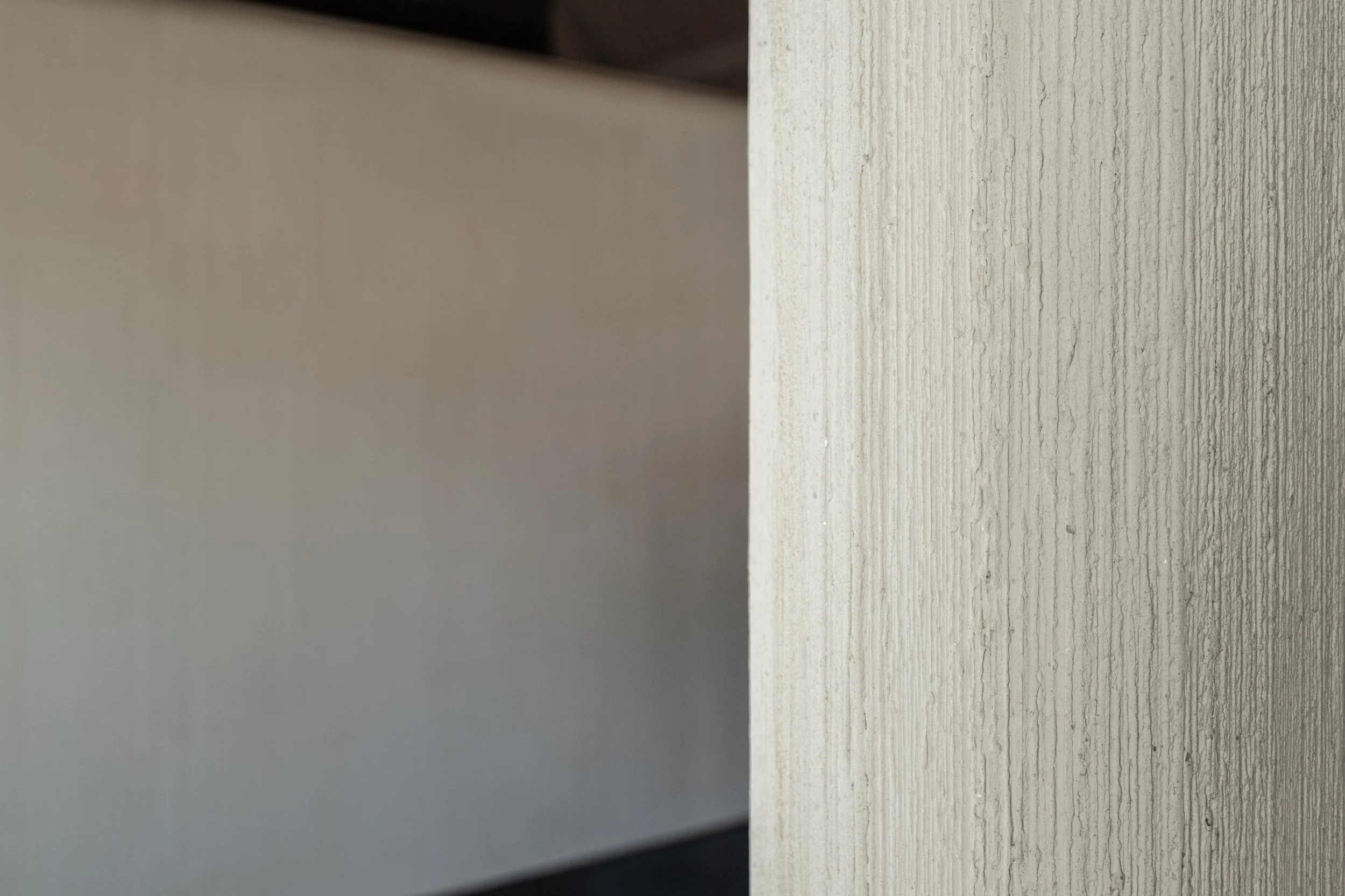 Close-up of a textured, light-colored wall with vertical grooves, and a black object or shadow at the top left corner.