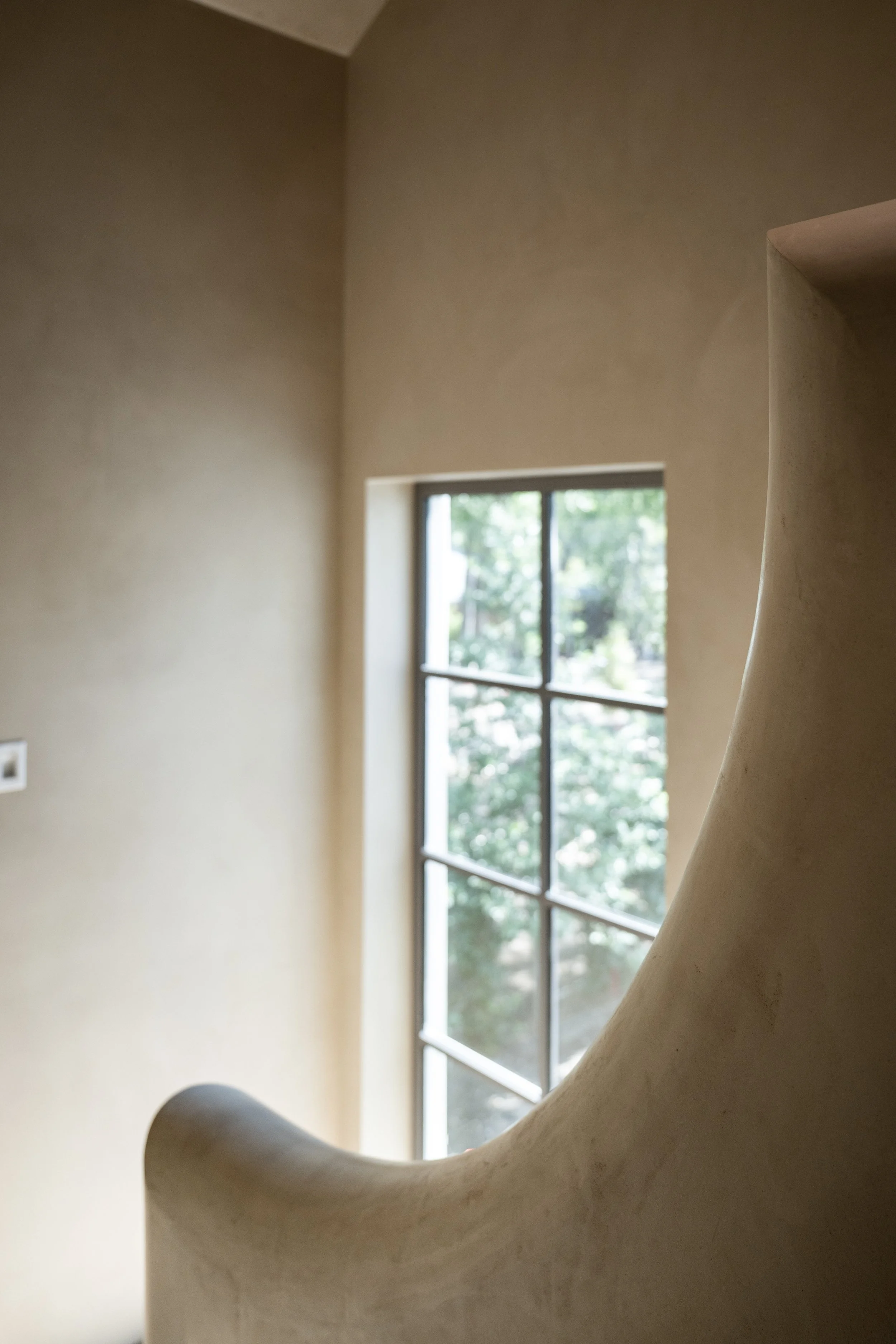 Close-up of a beige, curved architectural feature in front of a window with trees outside, in a room with beige walls.
