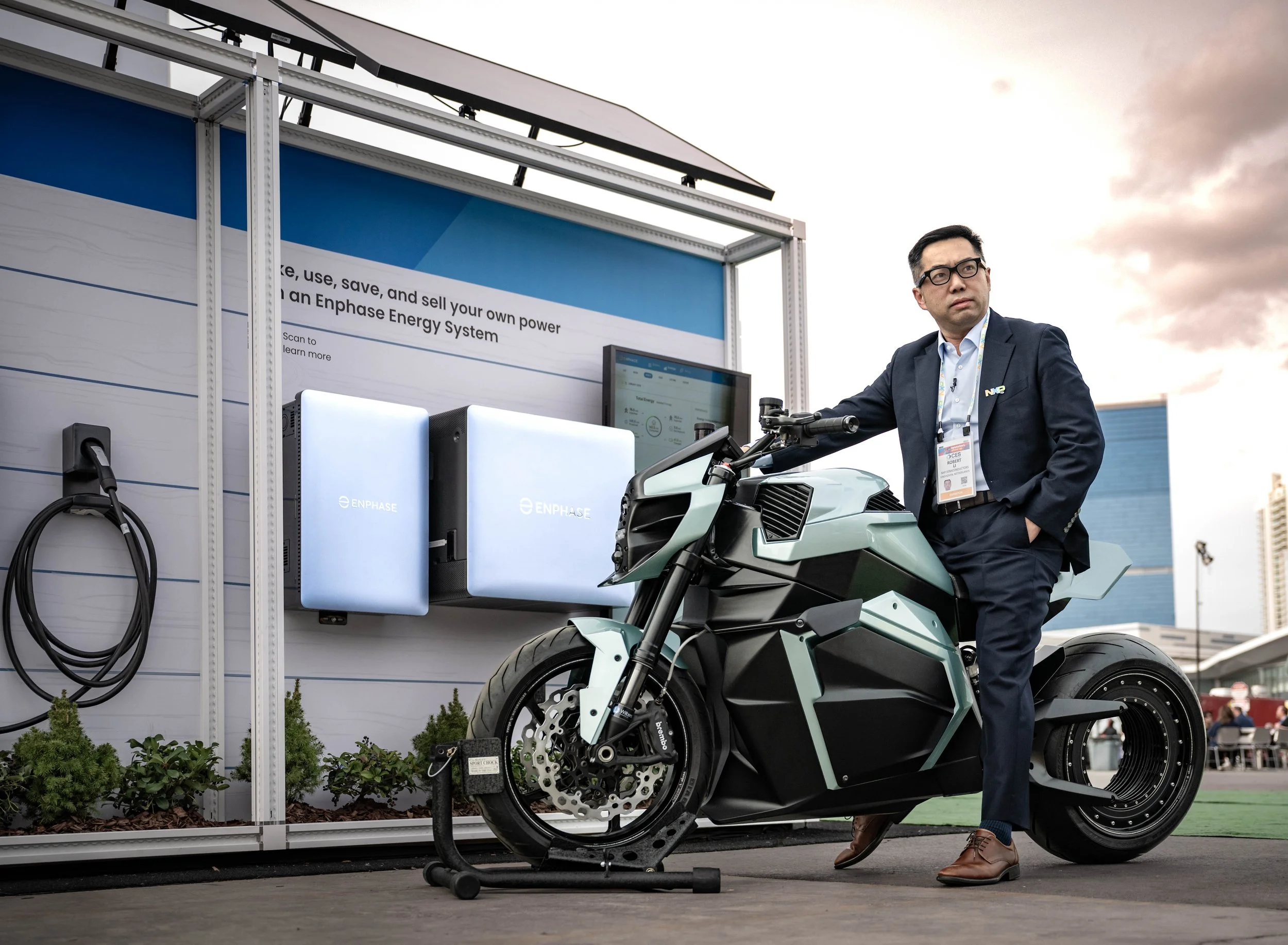 A man in a business suit standing beside an electric motorcycle at an energy exhibition, with a display booth and solar panels in the background.