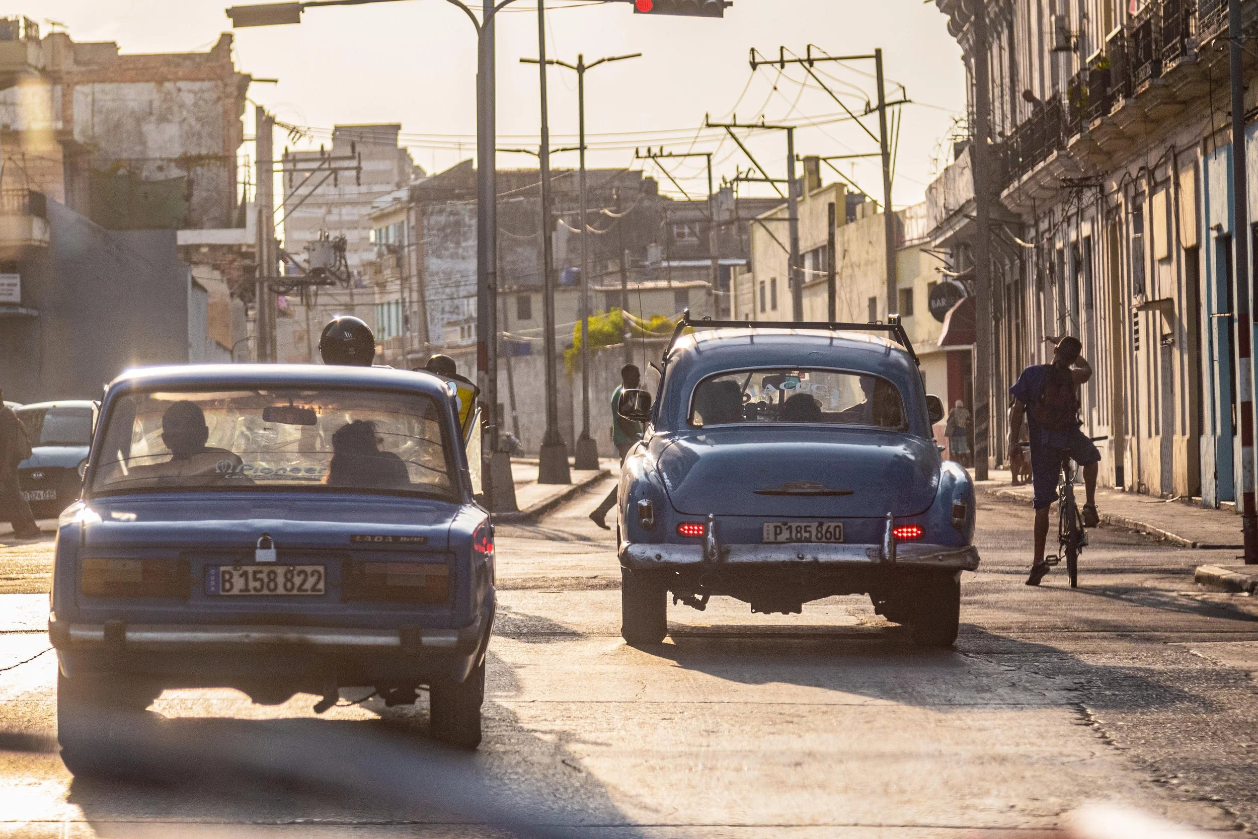 Street scene with vintage cars, cyclist, and people in urban area at sunset.