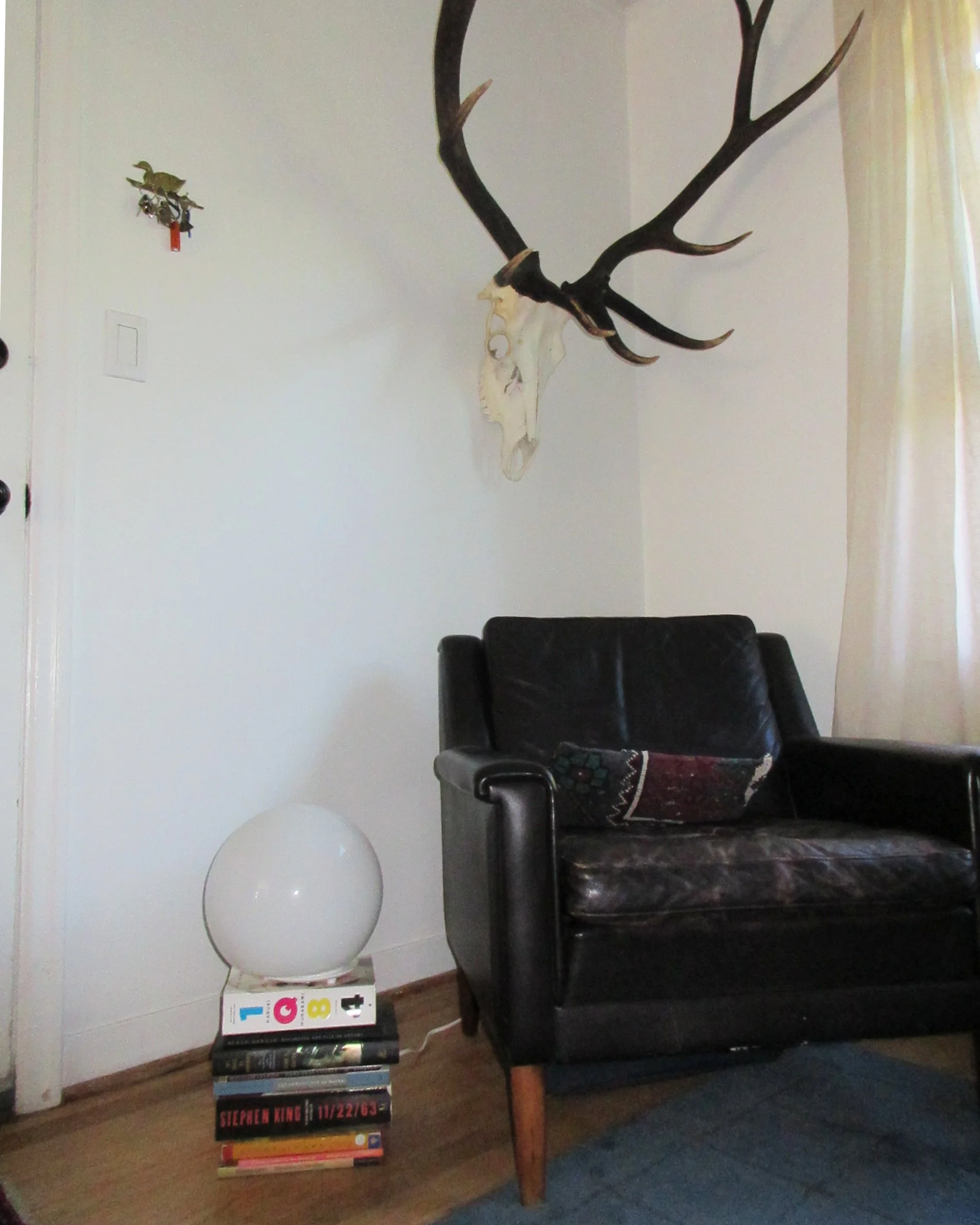 elk antlers rest over sadie’s reading chair. her 2026 has-reads stack up on the floor.