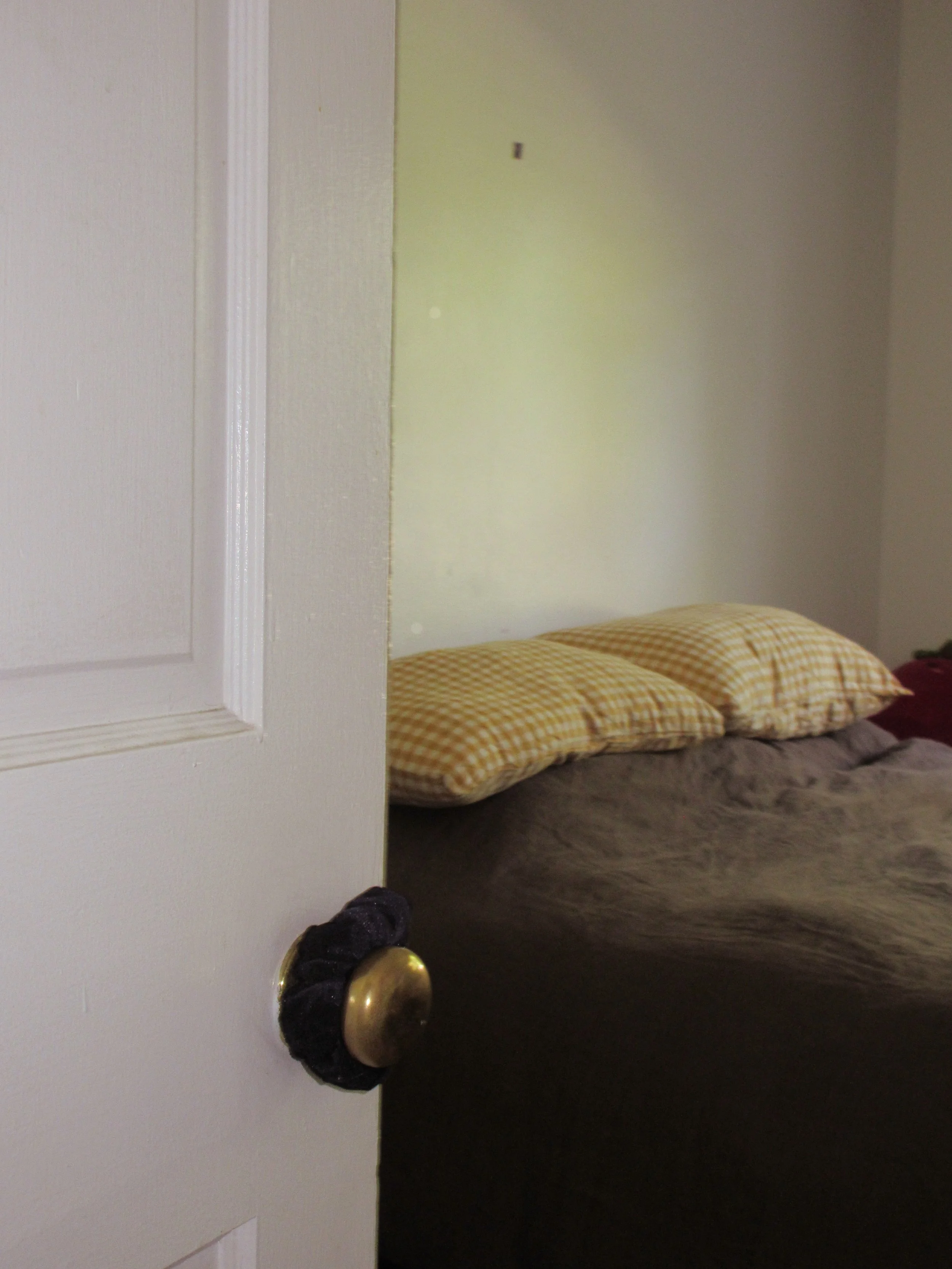 a peek into the bedroom, welcomed by a scrunchie on the door handle. they wanted a comically small piece of art above the bed, put a stamp there as a placeholder and it became the comically small piece of art.