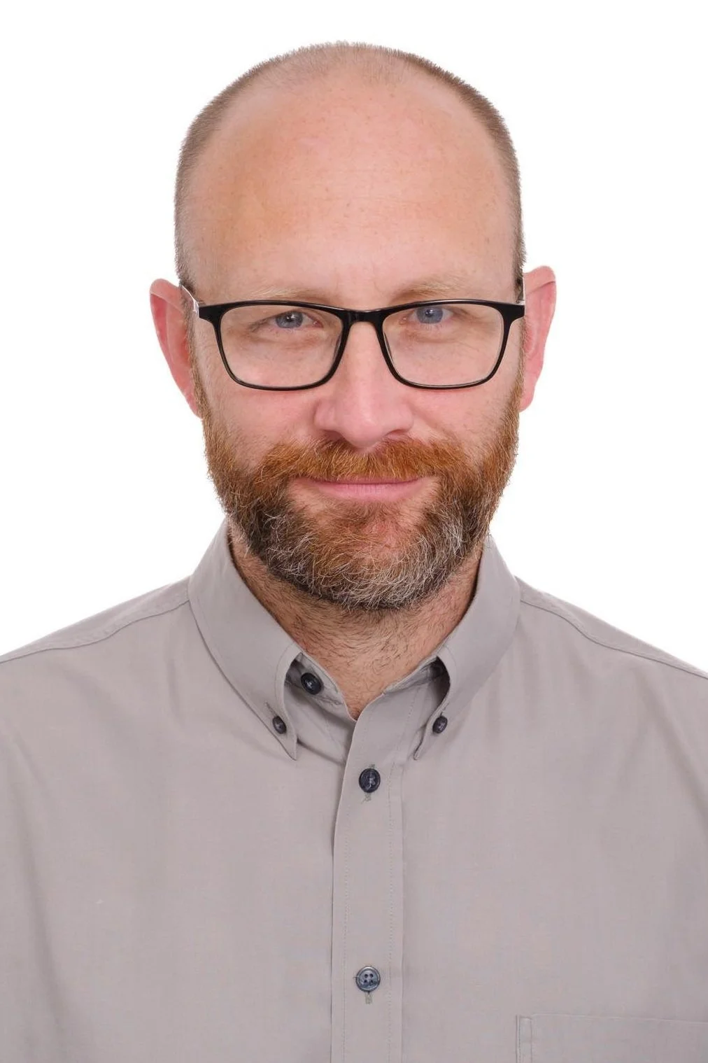 Portrait of a middle-aged man with a beard wearing black-framed glasses and a light gray button-down shirt against a white background.