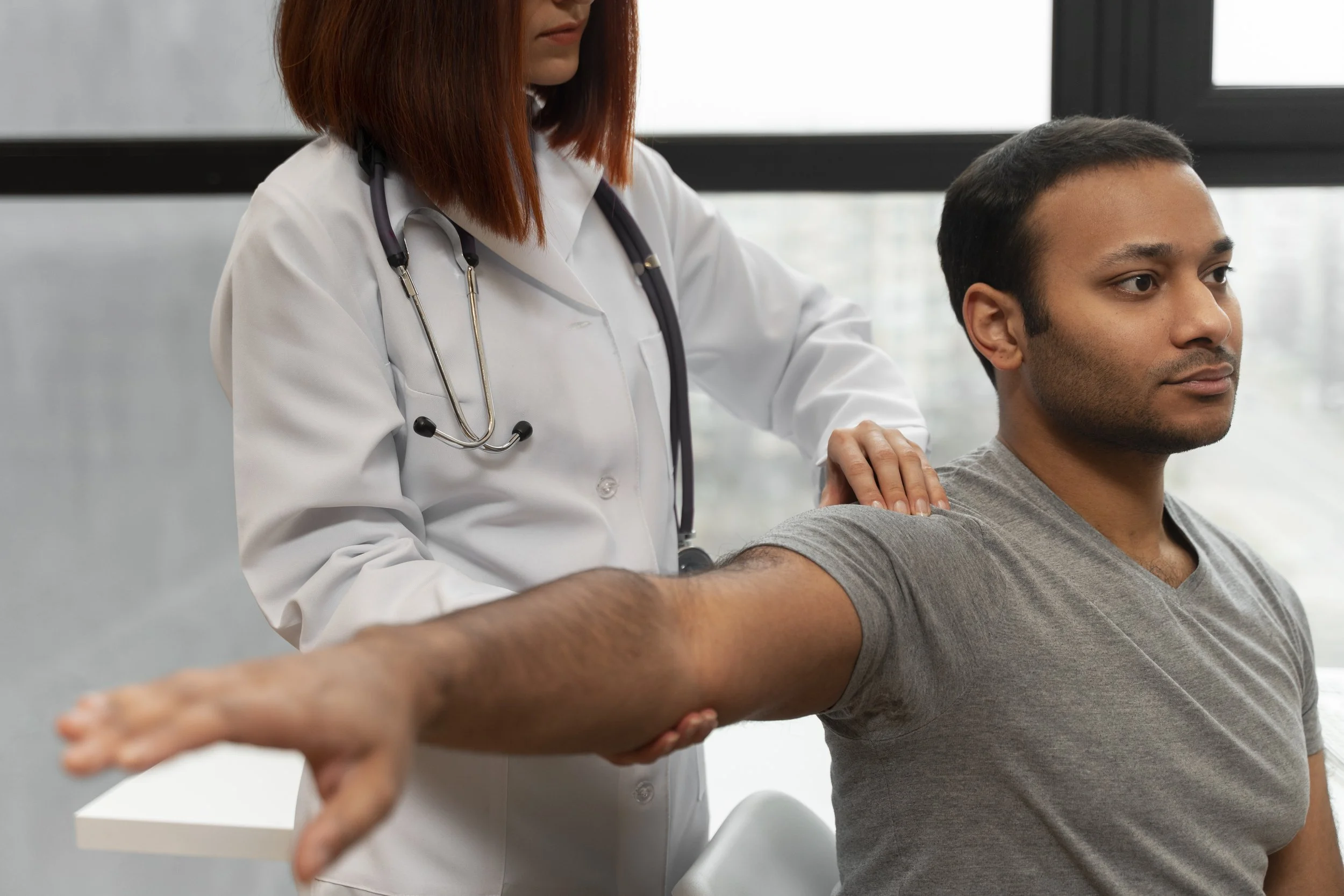 A doctor performing a physical examination on a man, testing his arm strength by stretching his arm outward.