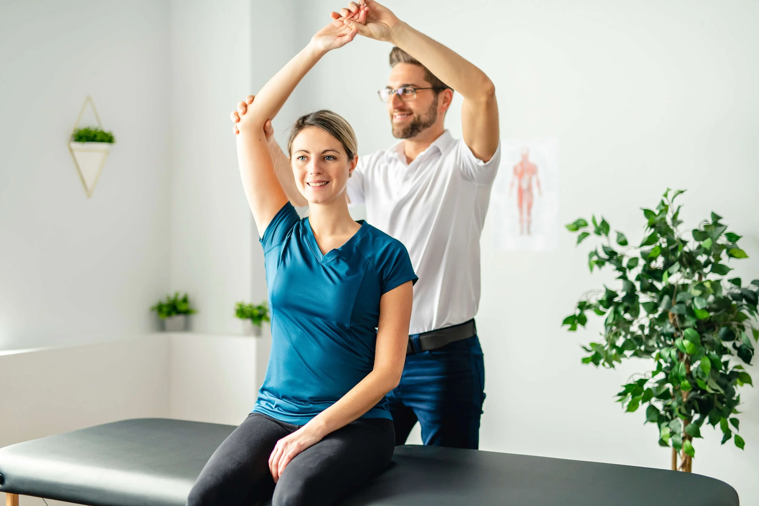 A physical therapist helping a woman stretch her shoulder while sitting on a therapy table in a medical office.
