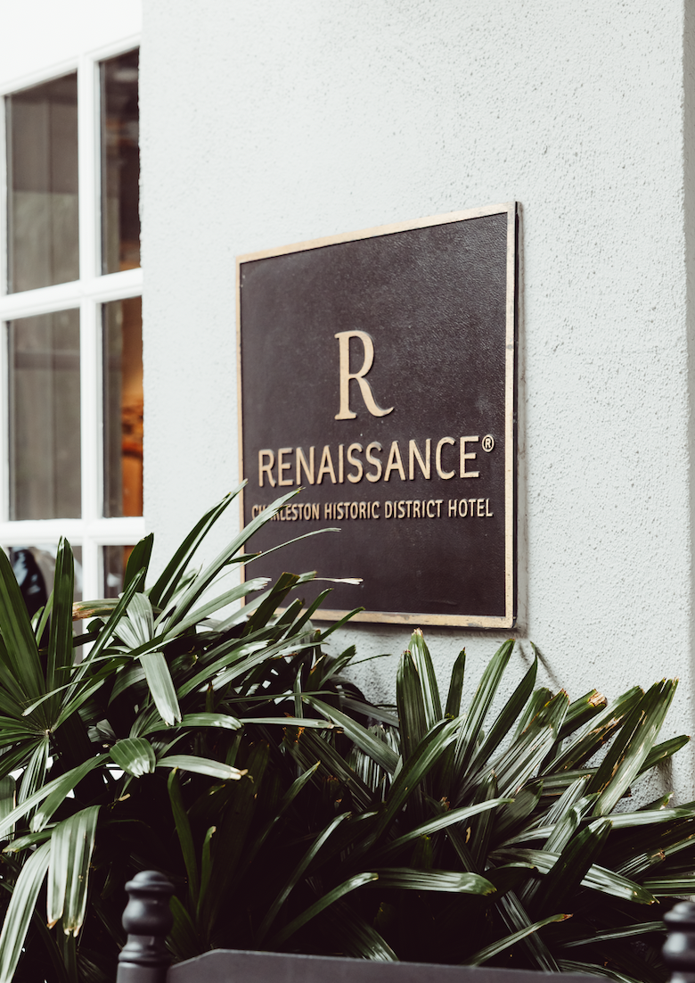 Hotel sign reading 'Renaissance Charleston Historic District Hotel' with green plants in front.
