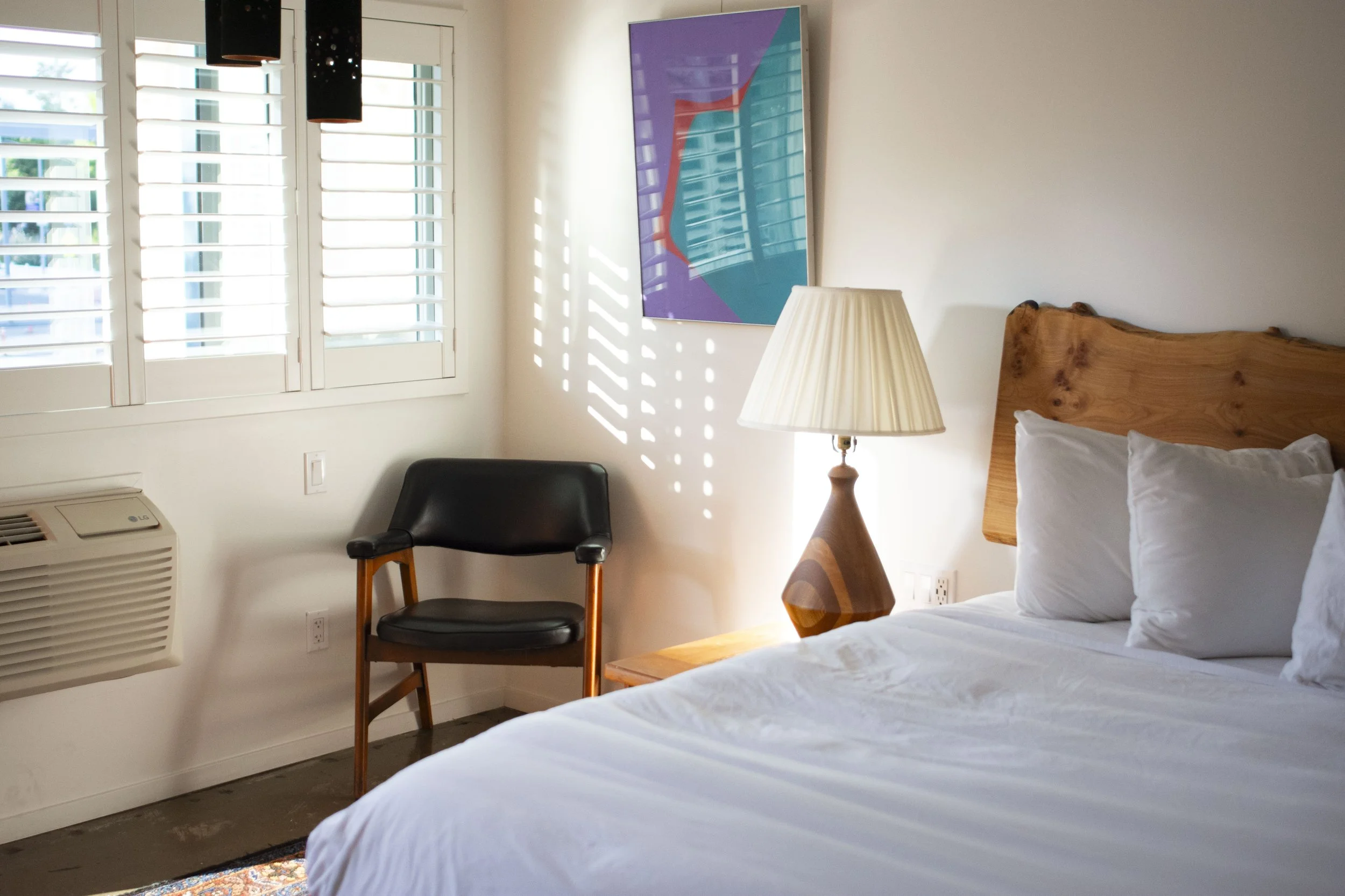 image shows a queen sized bed with lamp and chair.
