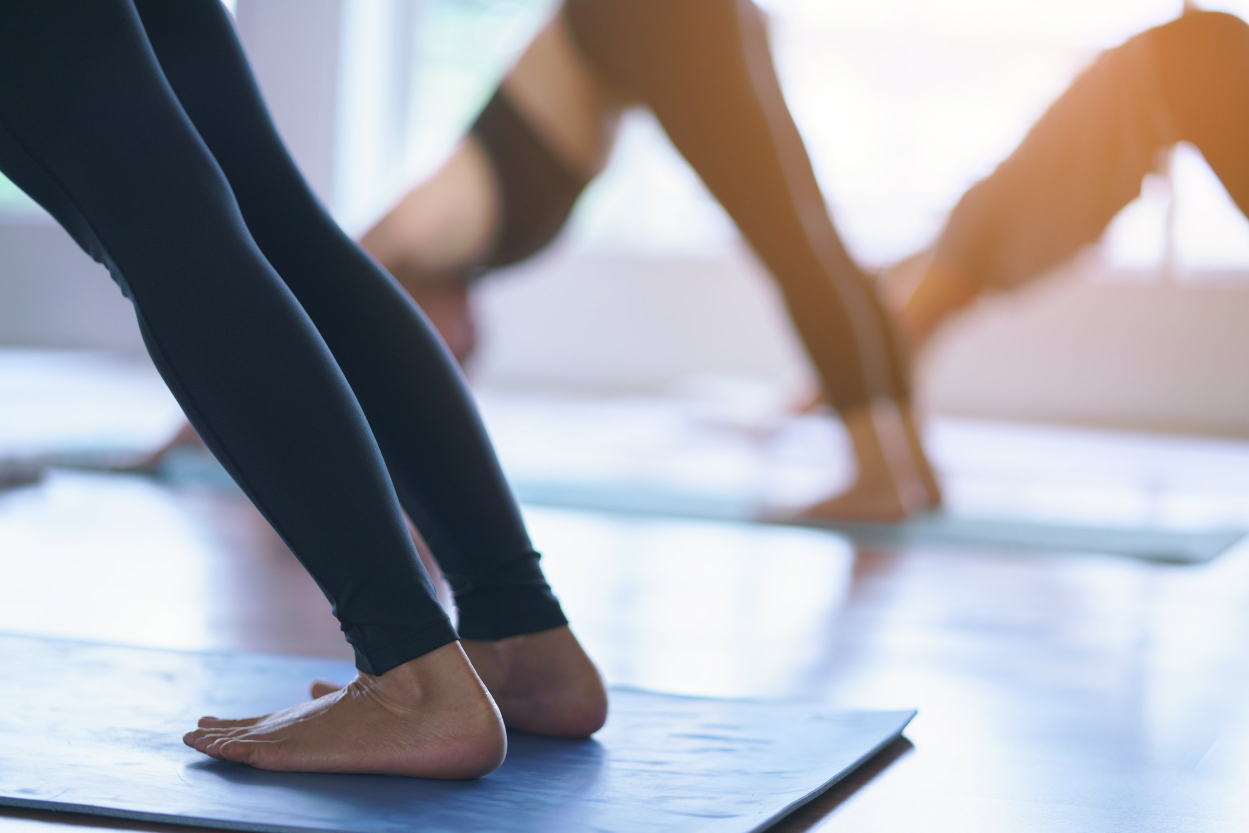 Close-up of a woman performing downward dog yoga pose on a mat in a bright room.