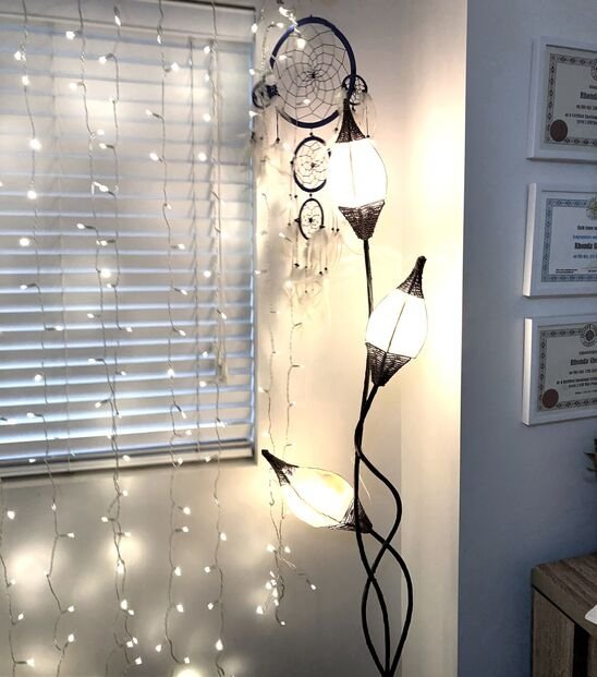 Room corner with decorative floor lamp, dreamcatcher, and string lights. Certificates are on the wall.